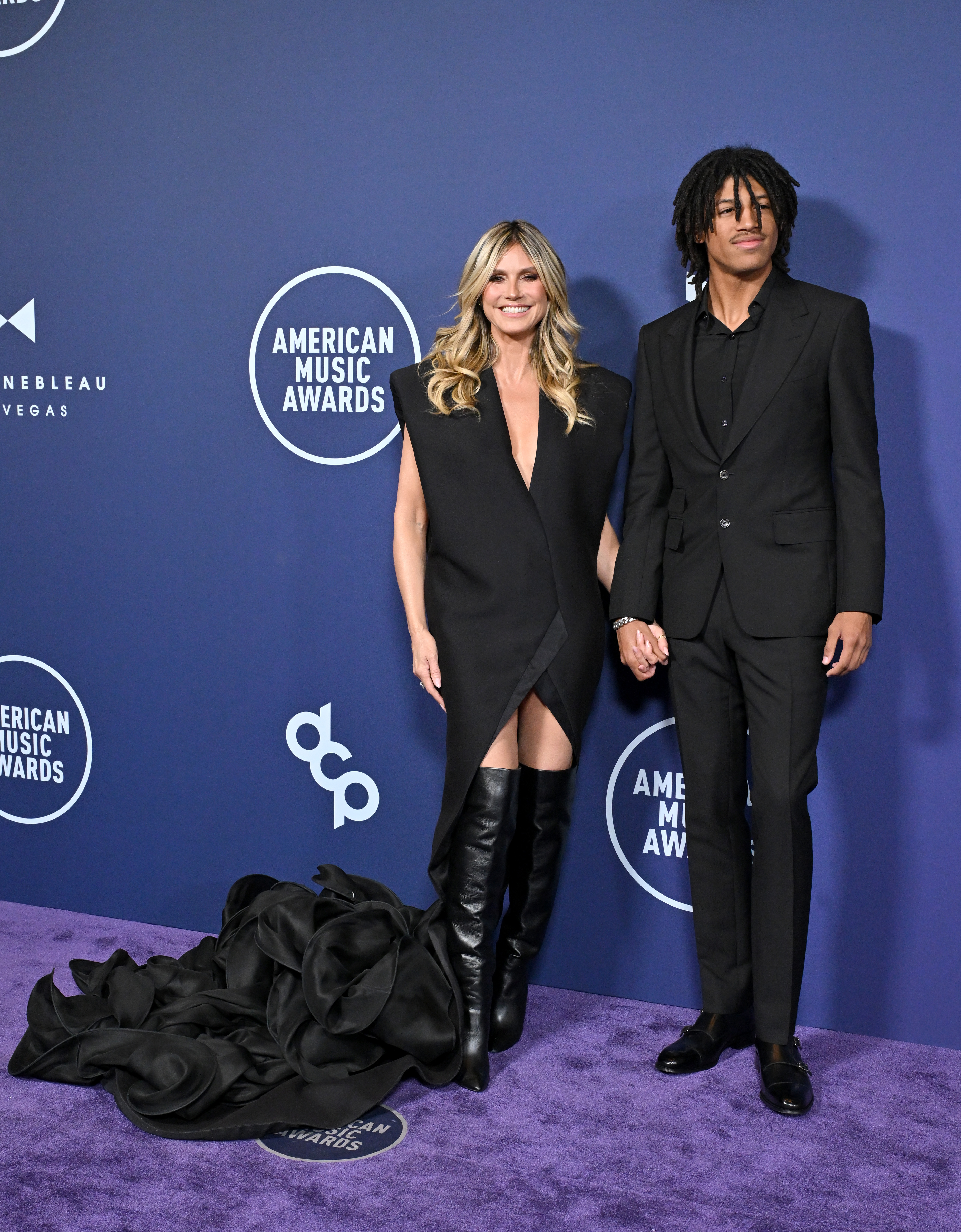 Henry Samuel and Heidi Klum hold hands as they face the cameras together. Henry looks off to the side with a calm, steady gaze, creating a contrast to the buzz of the carpet around them.