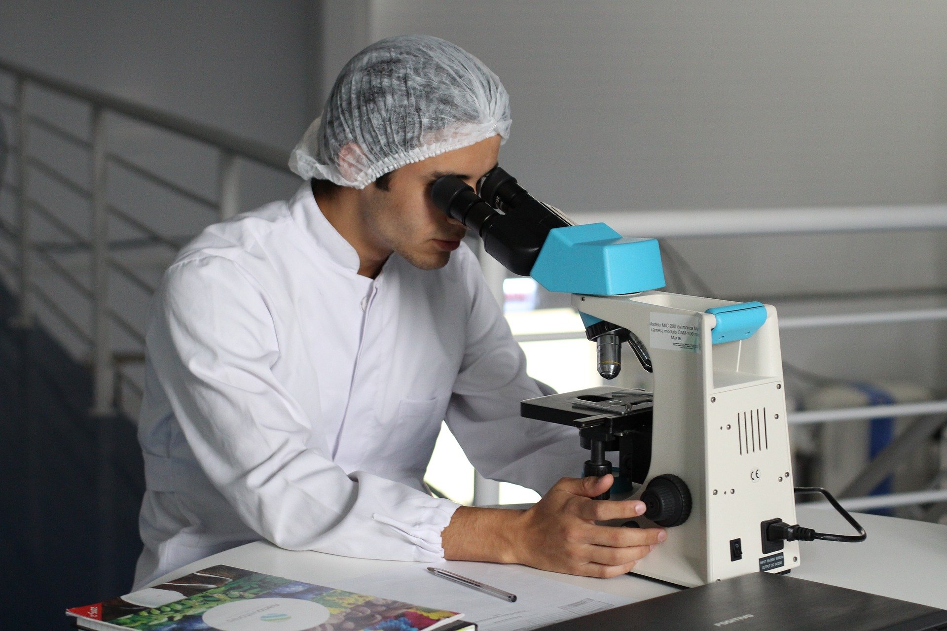 A scientist wearing their work scrubs while looking through a microscope | Photo: Pixabay/luvqs