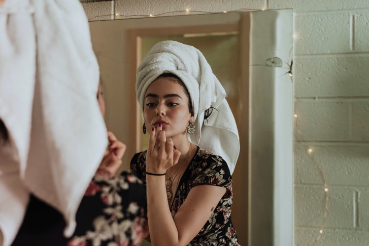 Une femme mettant un rouge à lèvre devant un miroir. | Photo : Unsplash