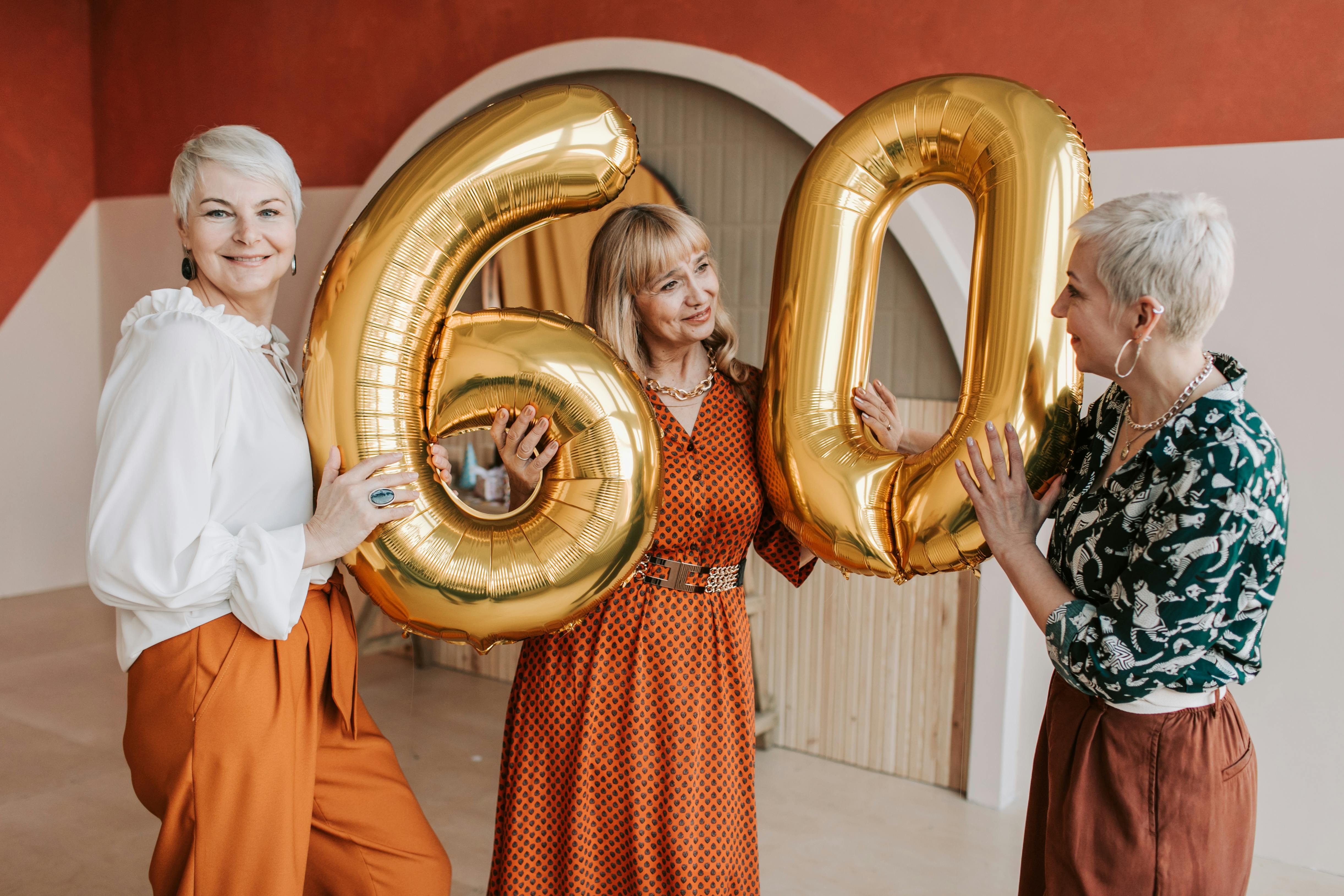 Three women holding up birthday balloons that write out the number "60" | Source: Pexels