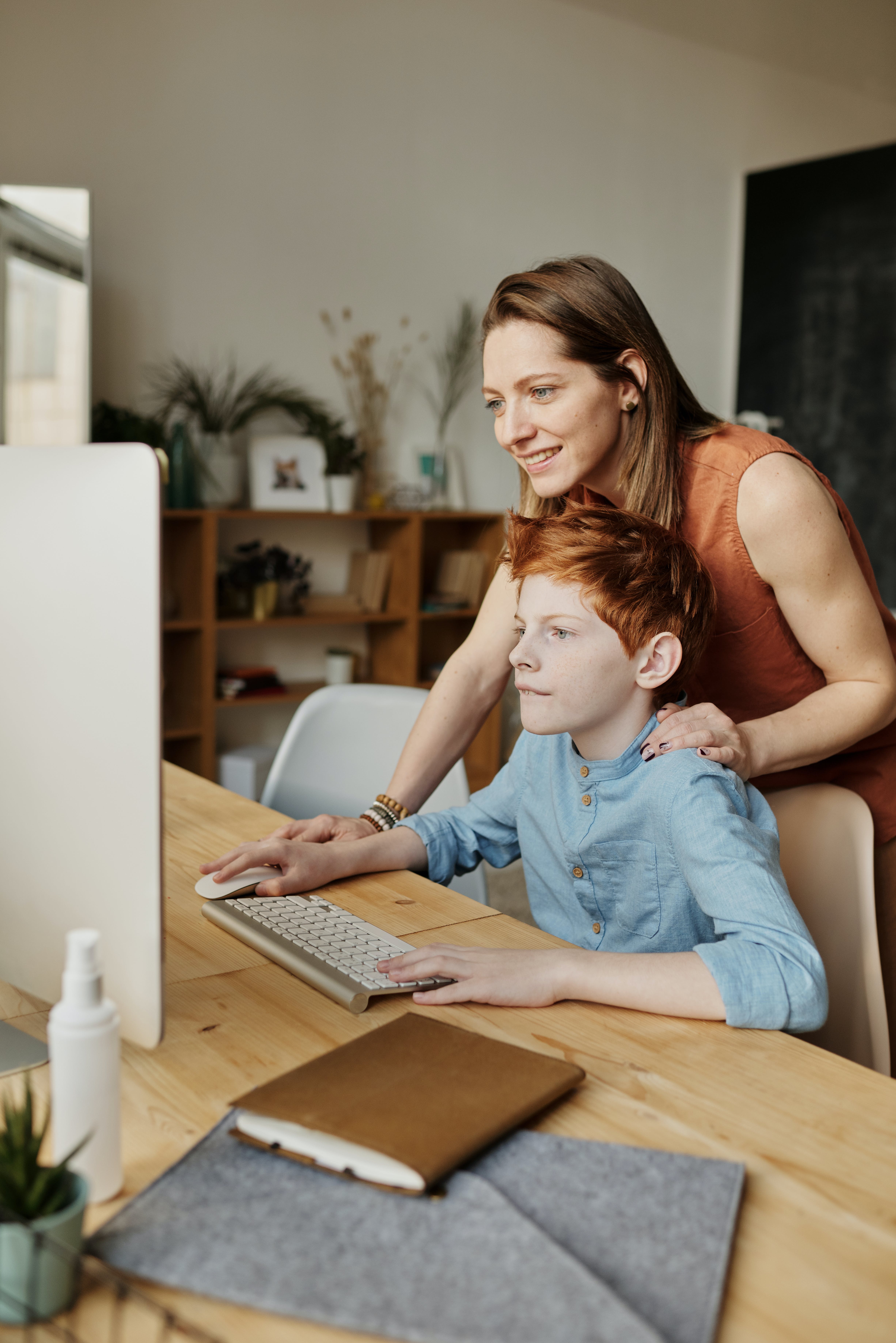 A woman bonding with a boy while using a personal computer | Source: Pexels