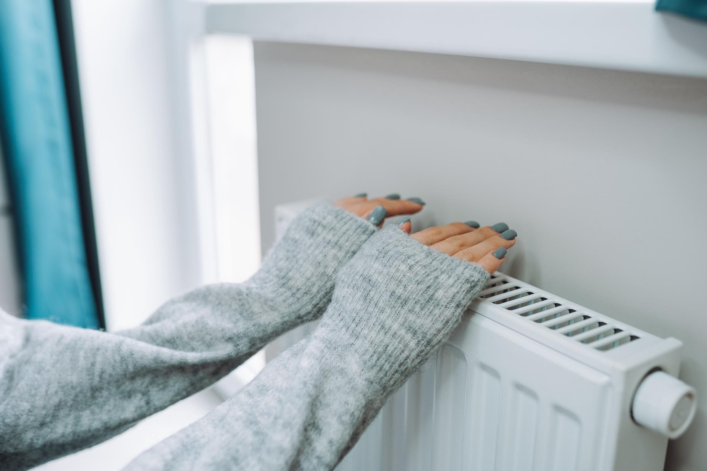 A woman warming her hands over a battery radiator | Source: Getty Images