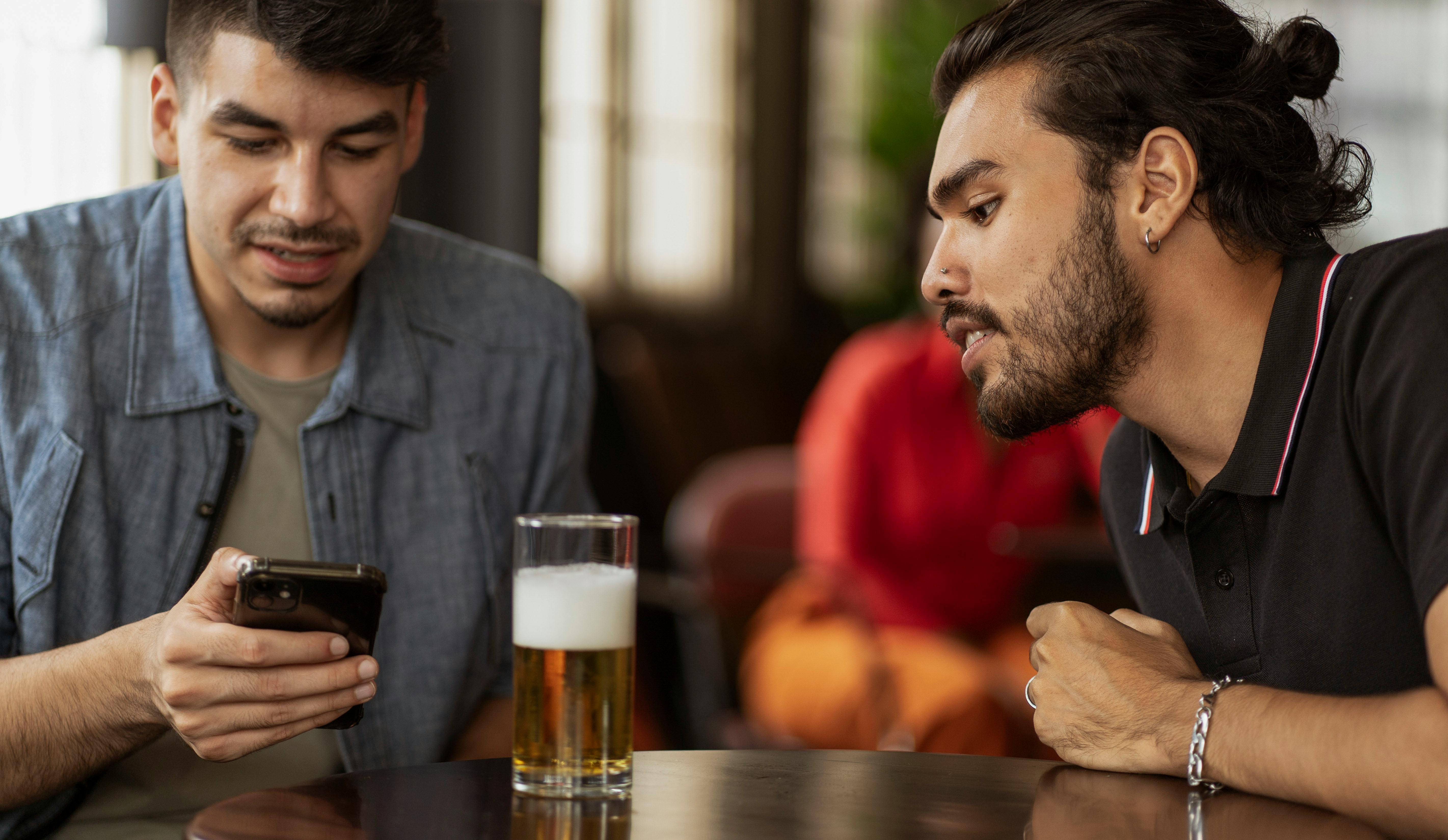 A man using a phone while another one looks over at a bar | Source: Pexels
