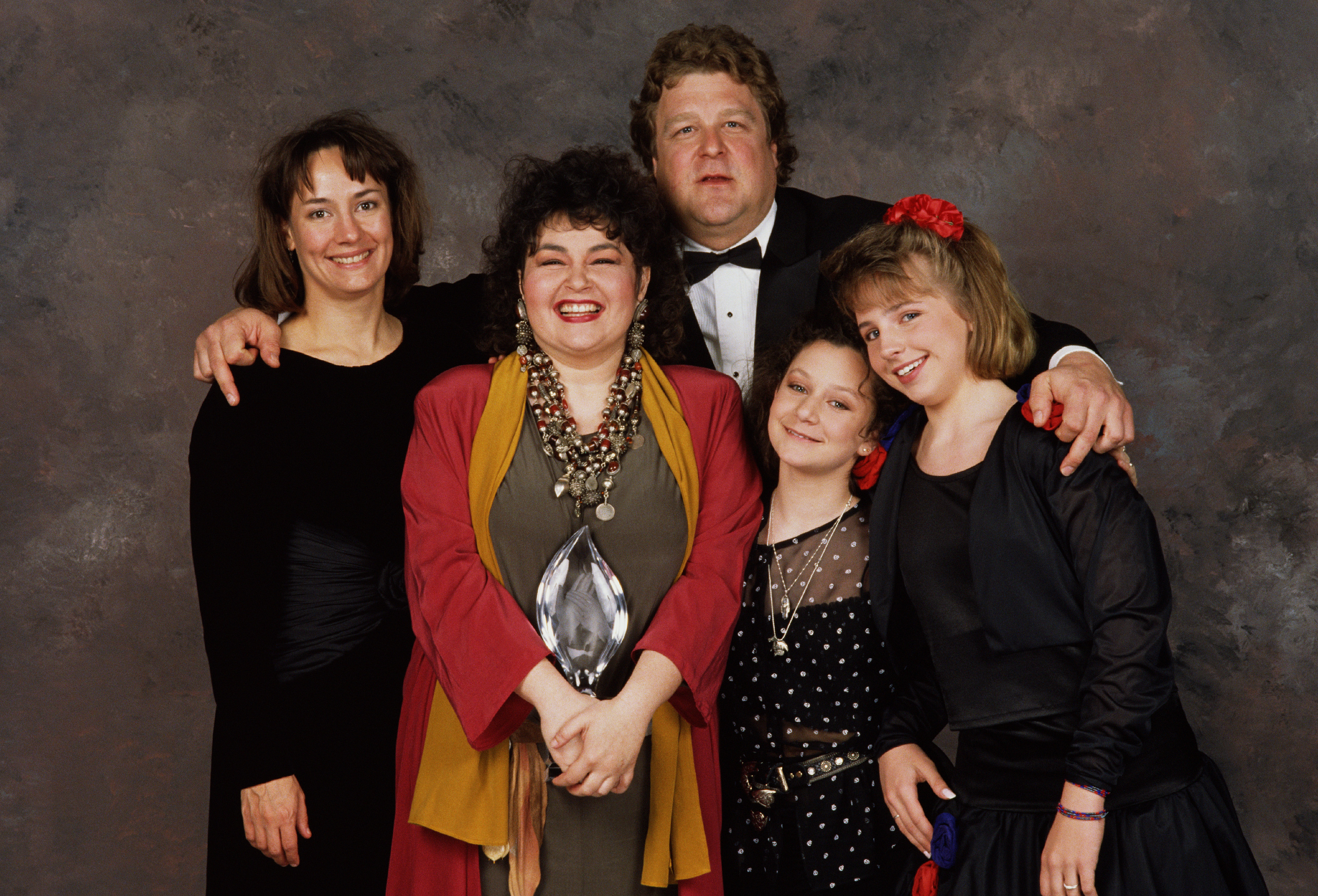 The cast of "Roseanne:" Laurie Metcalf, Roseanne Barr, John Goodman, Sara Gilbert, and Lecy Goranson, pose backstage in Beverly Hills, California, after winning the 1989 People's Choice Award for the Best TV Comedy | Source: Getty Images