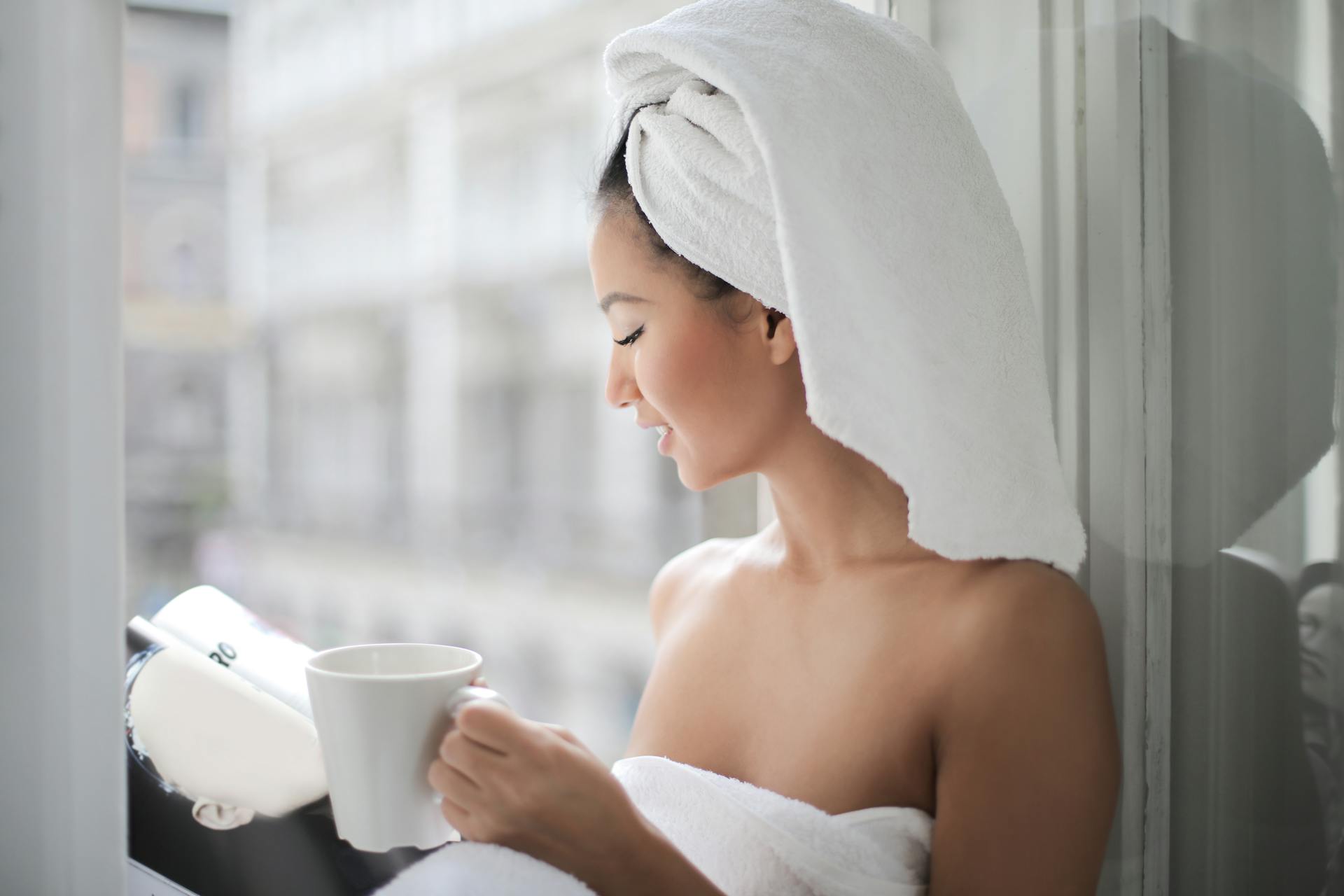 A woman reading a magazine and holding a mug near a glass window | Source: Pexels