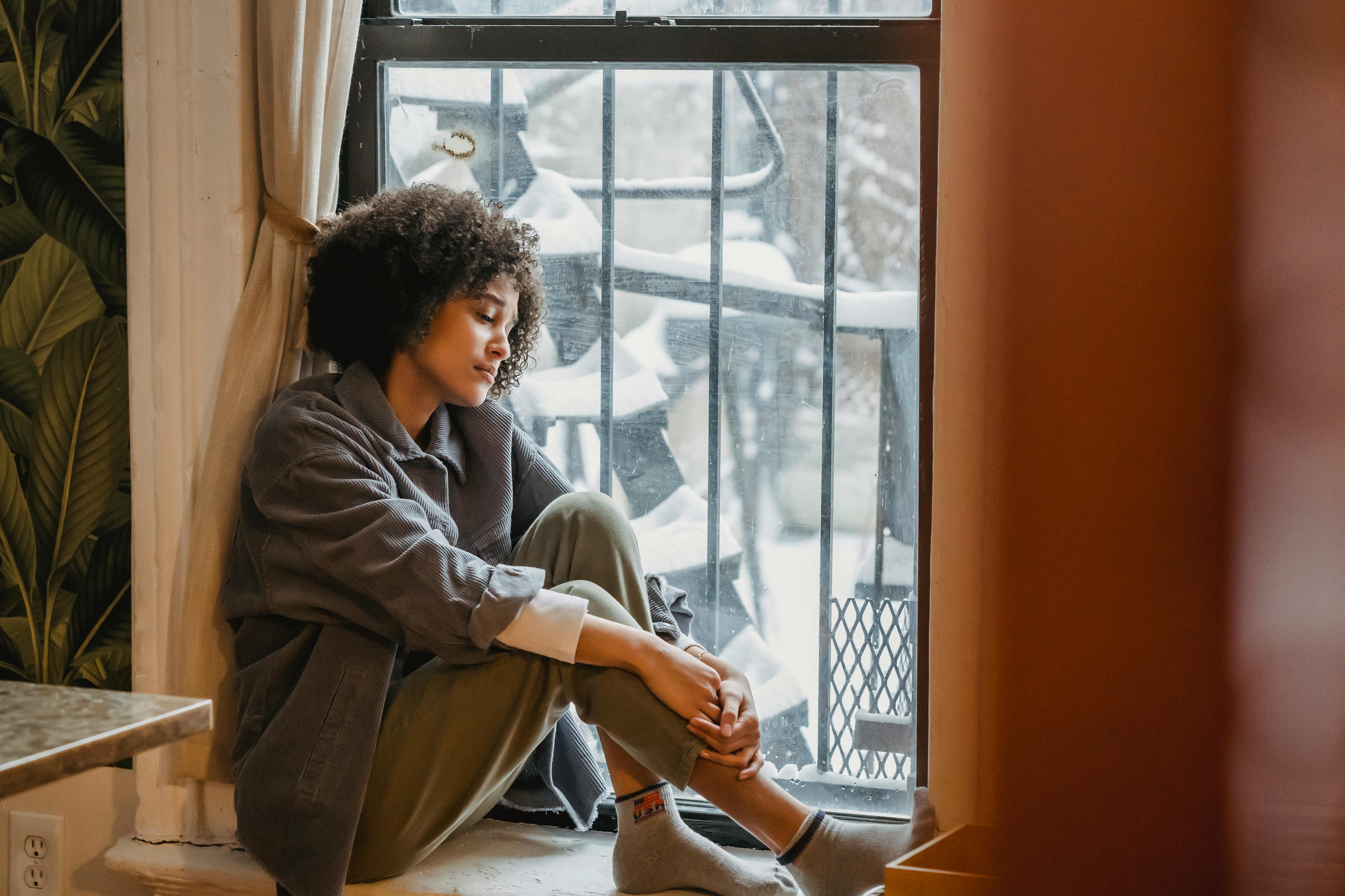 A woman sitting by a window contemplating her life | Source: Pexels