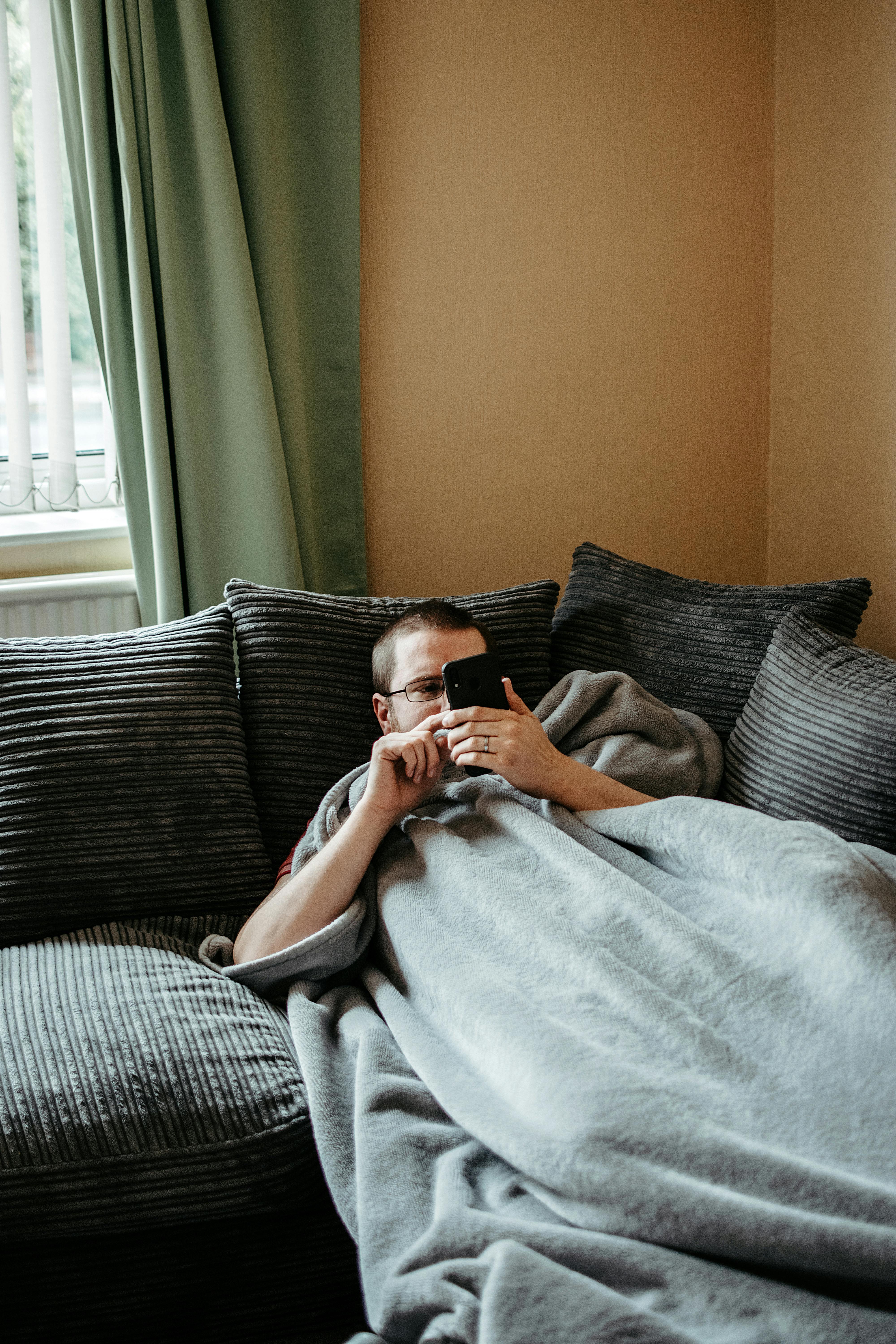 A man lazying around on a couch while using his phone | Source: Pexels