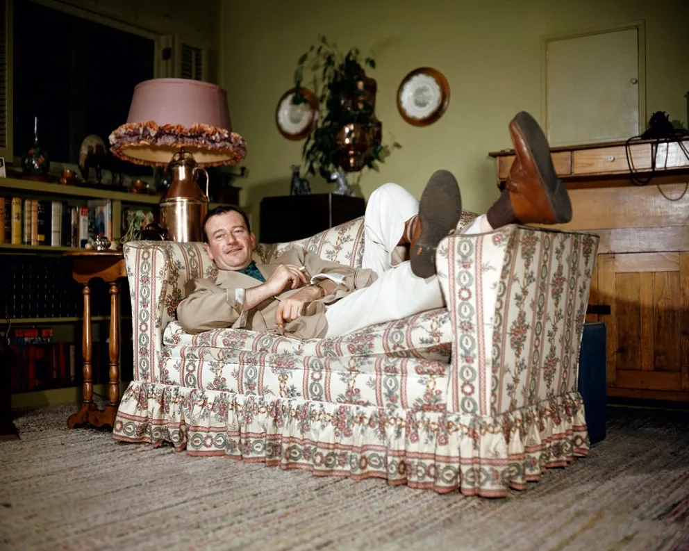 Portrait of American actor John Wayne (1907 - 1979), a cigarette in one hand, as he relaxes, feet up on the arm of a couch, 1950s. | Source: Getty Images