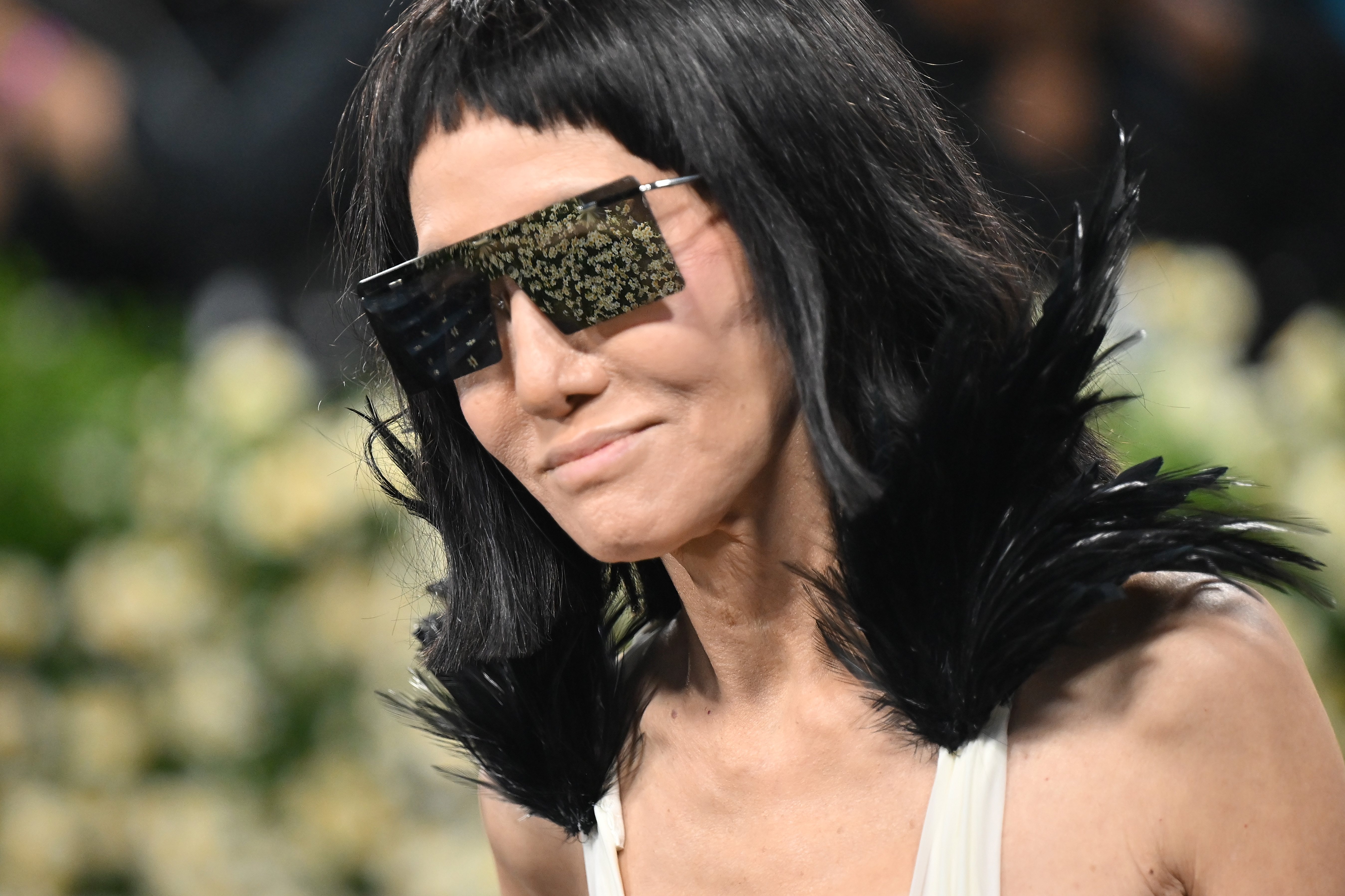 Vera Wang wears oversized reflective sunglasses and a jet-black feathered collar as she arrives, giving a close look at the bold details of her custom ensemble.
