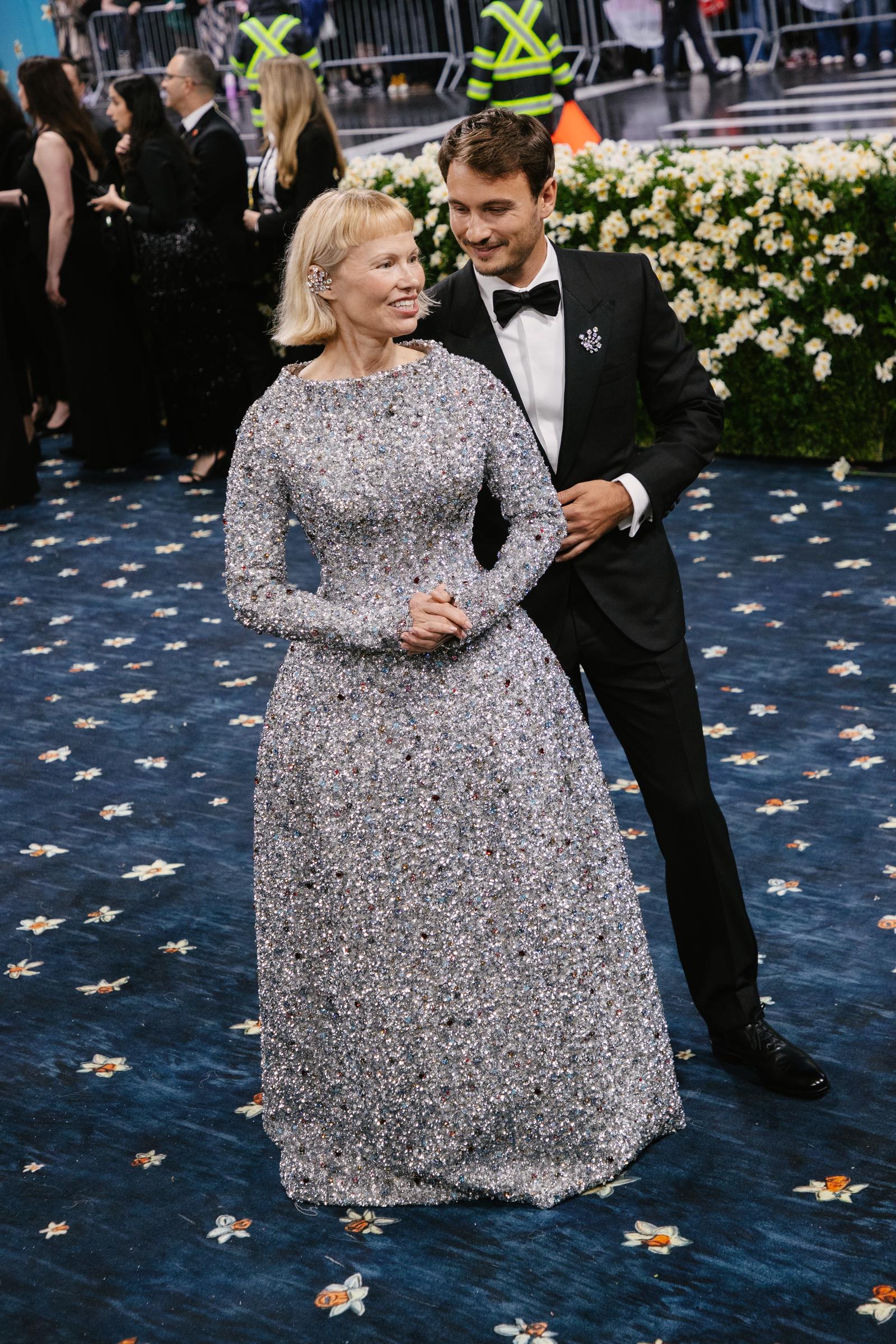 Sharing a candid moment, Pamela Anderson smiles alongside her son Brandon Thomas Lee on the Met Gala carpet. Their warm exchange added a touch of familial charm to the high-fashion celebration at the Metropolitan Museum of Art.