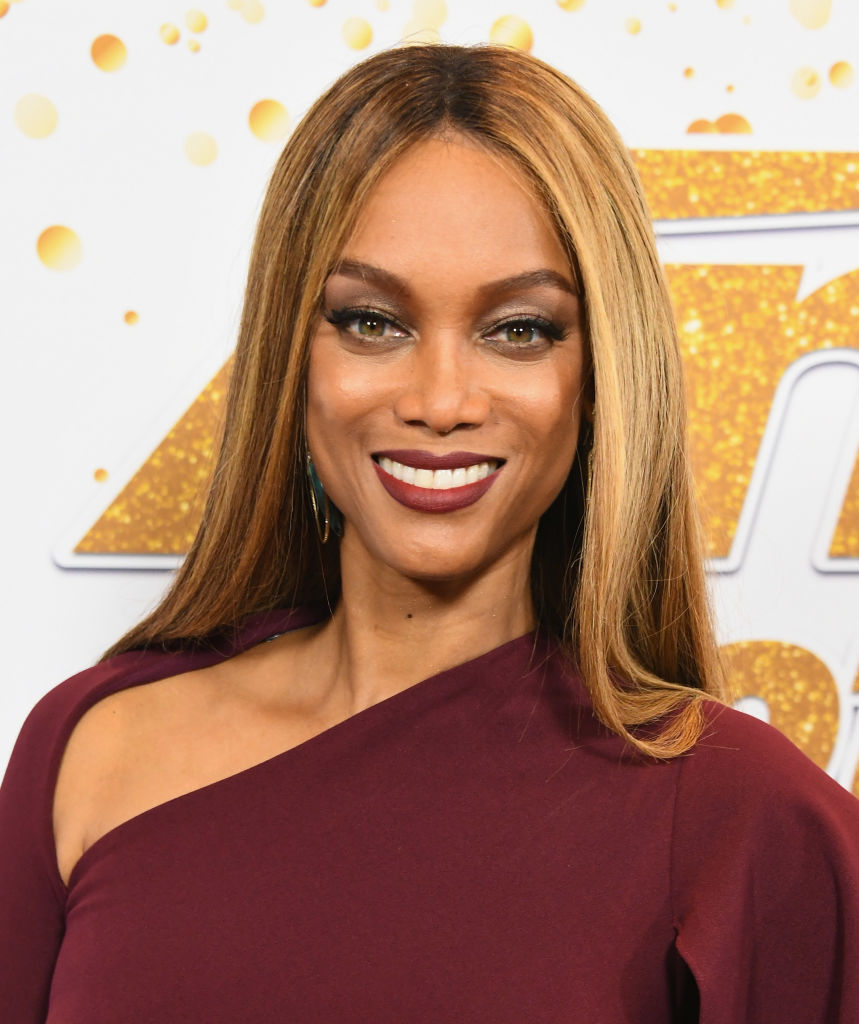 Tyra Banks stepped onto the "America's Got Talent" Season 13 red carpet in a one-shoulder burgundy dress, her honey-blonde hair framing a radiant smile with bold eyeliner and deep berry lipstick completing the striking look.