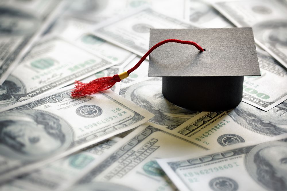 Graduation mortar board cap on top of one hundred dollar bills. | Source: Shutterstock