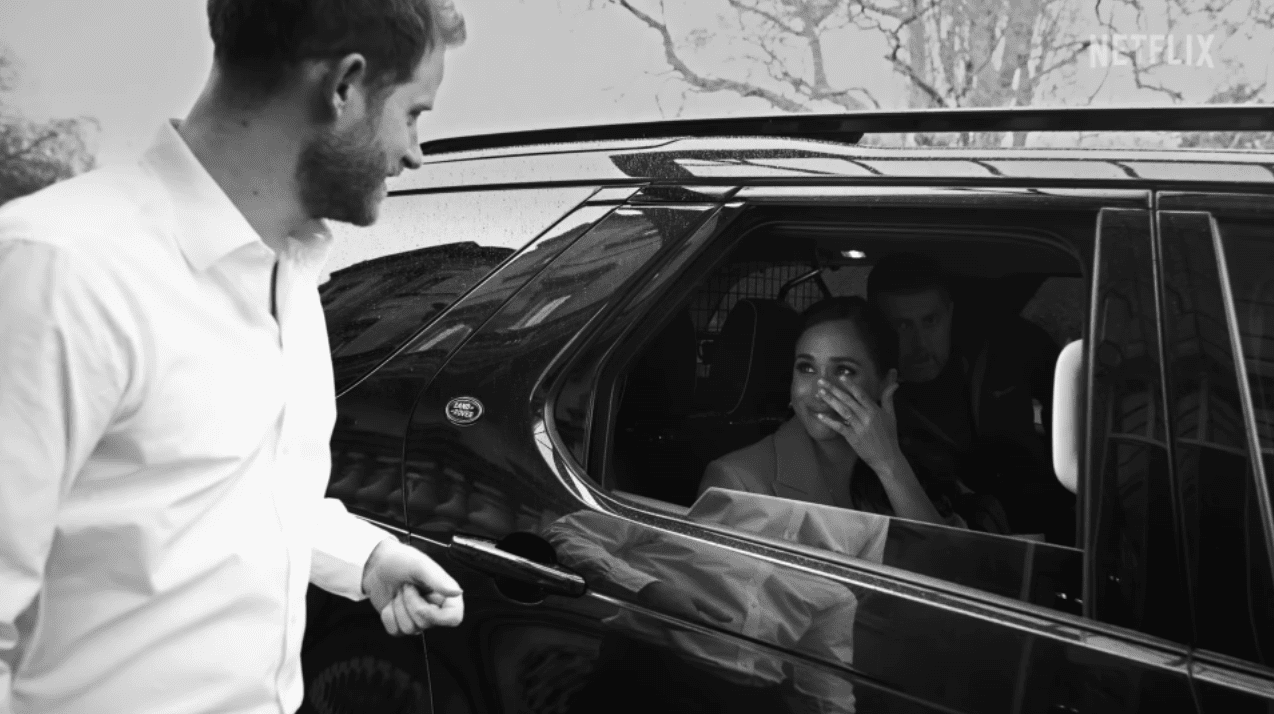 Meghan smiles up at Harry from the back seat of a car as she wipes away tears | Source: youtube.com/netflix