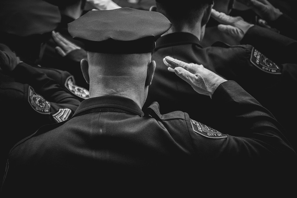 A black-and-white picture of police officers giving a hand salute to their fallen colleague. | Photo: Pixabay