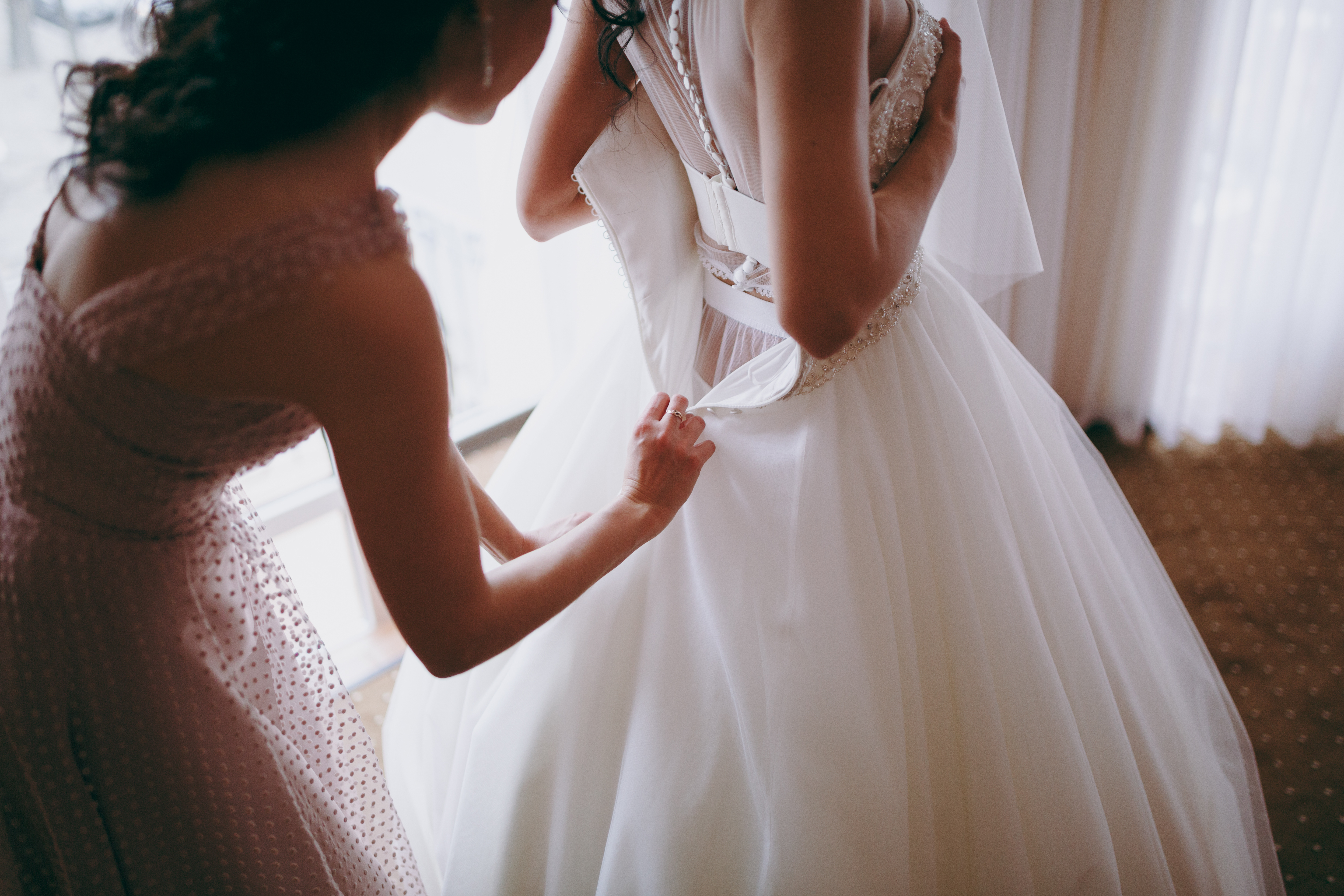 A woman helping a bride put on her bridal dress | Source: Shutterstock