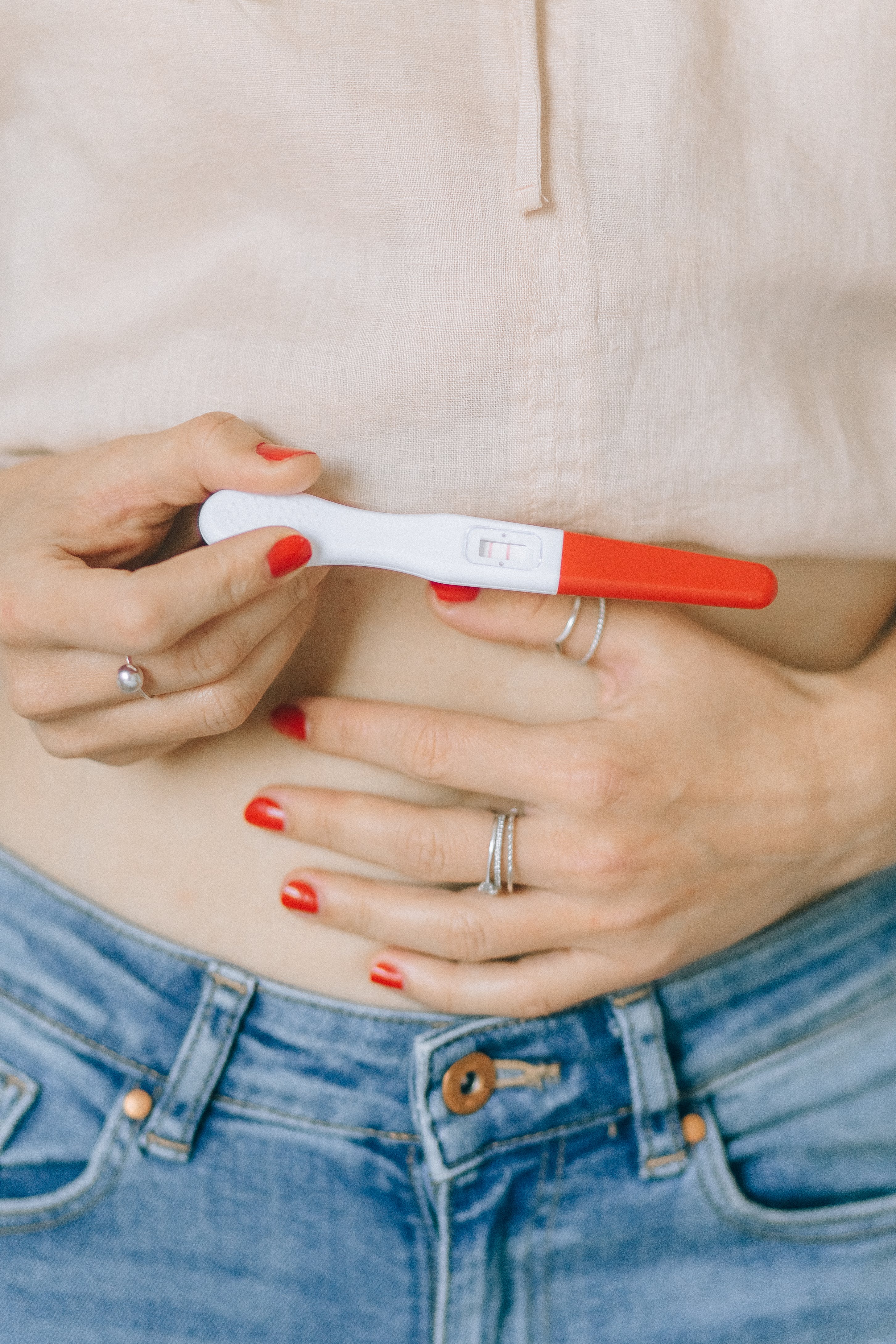 A woman holding her stomach and a pregnancy test | Source: Pexels