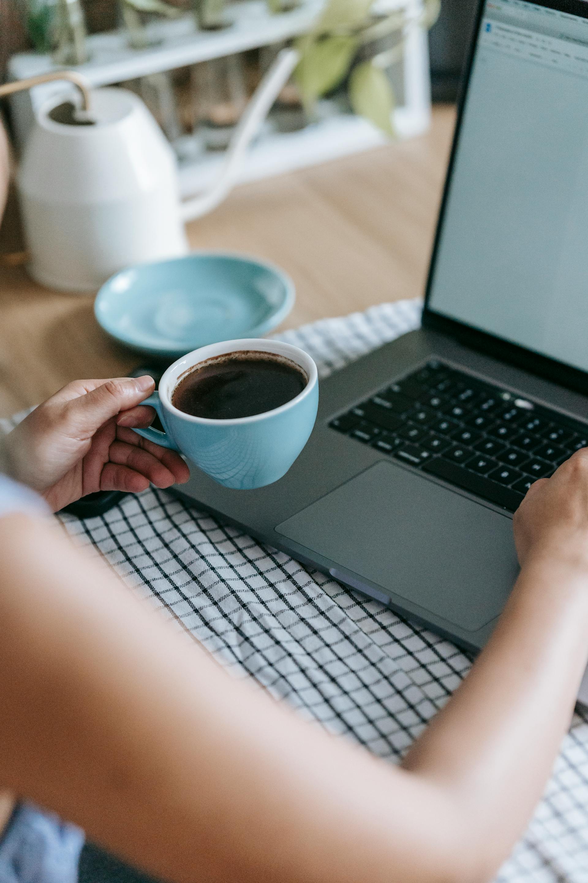 A woman holding a cup of coffee while using her laptop | Source: Pexels