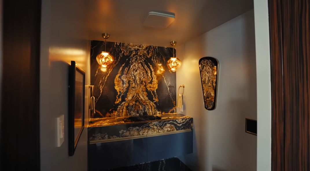 The powder room proves subtle stone was never really part of the brief. Golden pendant lights intensify the black-and-gold veining, turning a compact room into a full design moment. | Source: YouTube/Architectural Digest