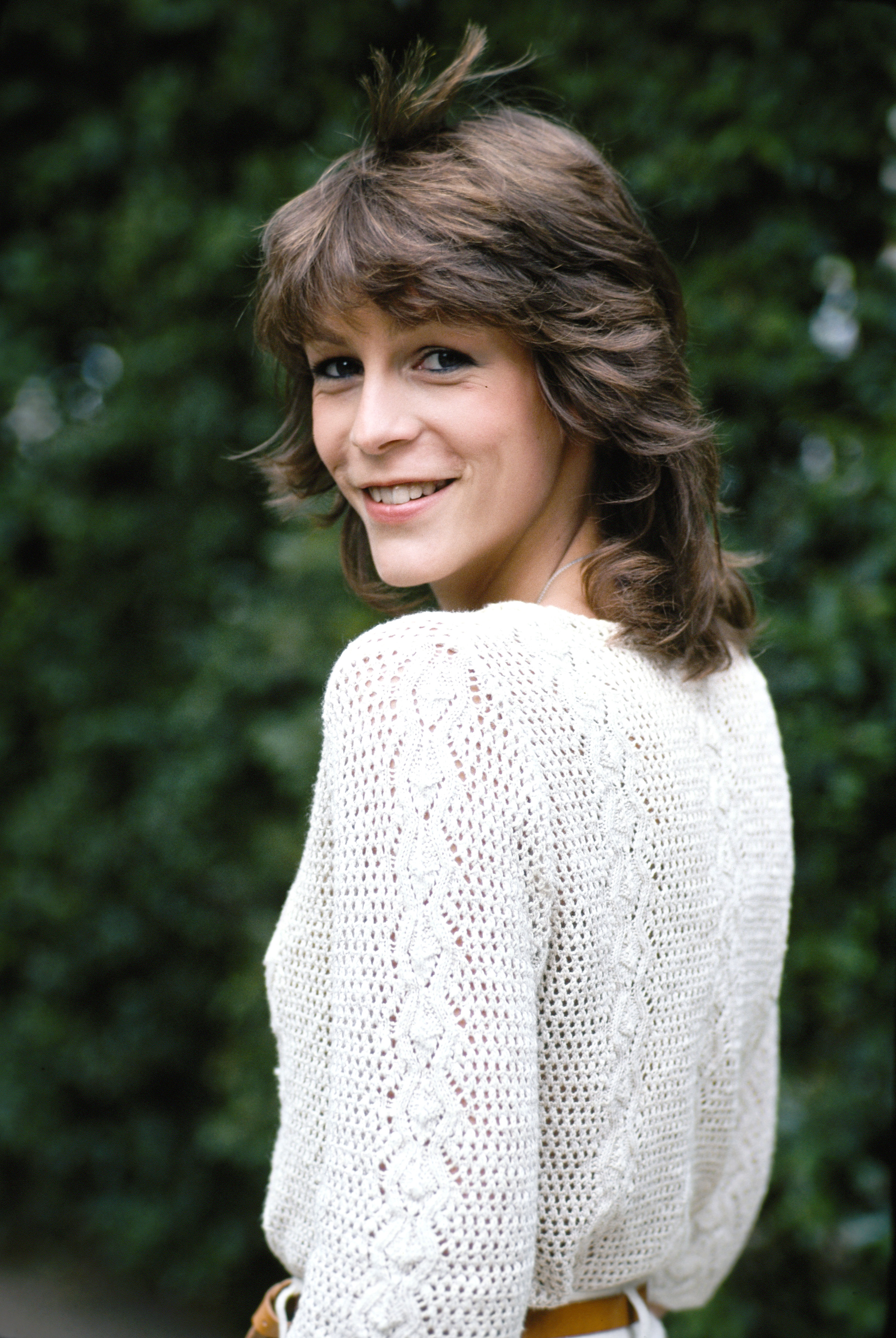 Jamie Lee Curtis flashes a soft smile while posing in a cream knit sweater at her Los Angeles apartment, captured in the early days of her Hollywood rise.