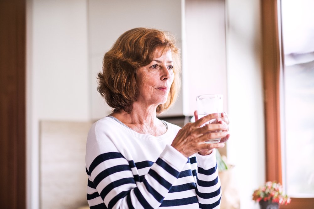 Mujer tomando una bebida mientras mira por la ventana. | Foto: Shutterstock