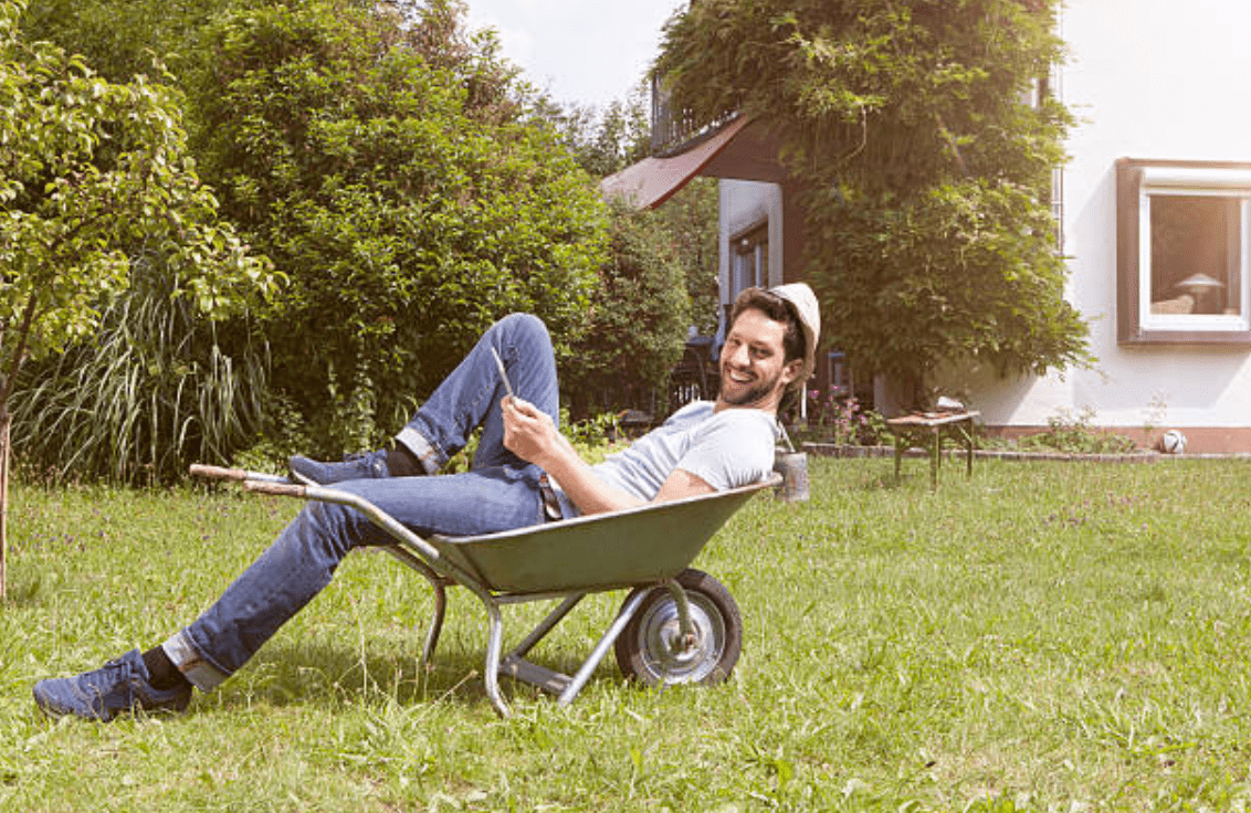 Smiling man lays in a wheelbarrow in a garden | Source: Getty Images