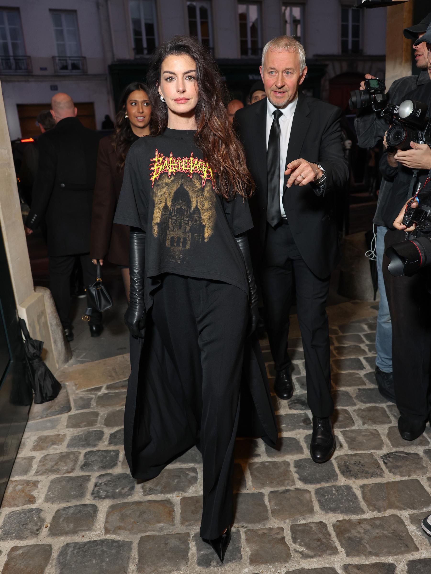 Anne Hathaway attended the Balenciaga Women’s Spring/Summer 2026 show at Paris Fashion Week in France. She wore a graphic T-shirt with a metal-inspired logo and a mullet-style design featuring a dramatic, flowing train. The look was completed with black trousers, leather gloves, and sharp, pointed shoes.