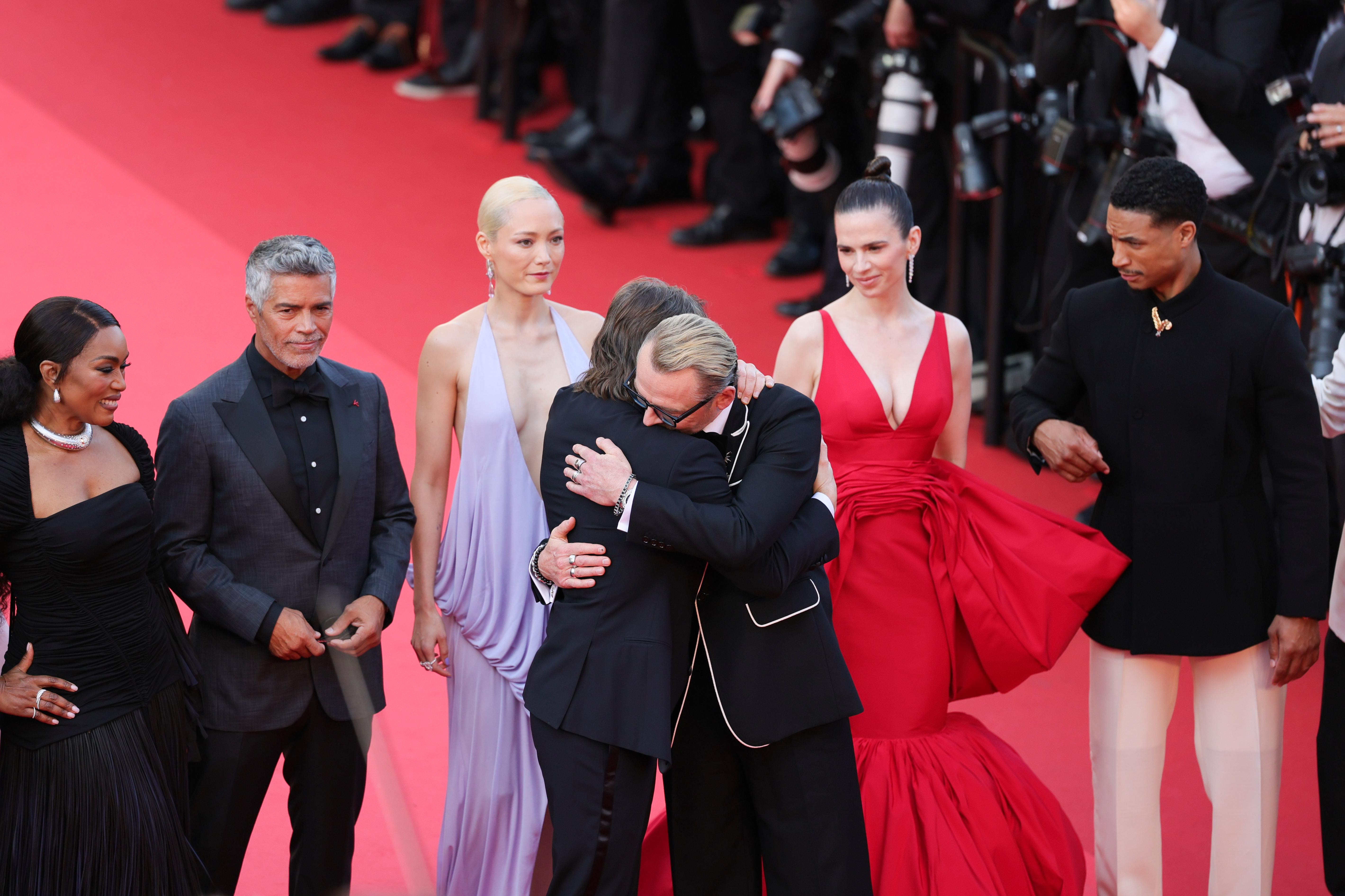 In an emotional moment on the red carpet, Tom Cruise embraces director Christopher McQuarrie while surrounded by cast members including Angela Bassett, Pom Klementieff, Hayley Atwell, and Greg Tarzan Davis.