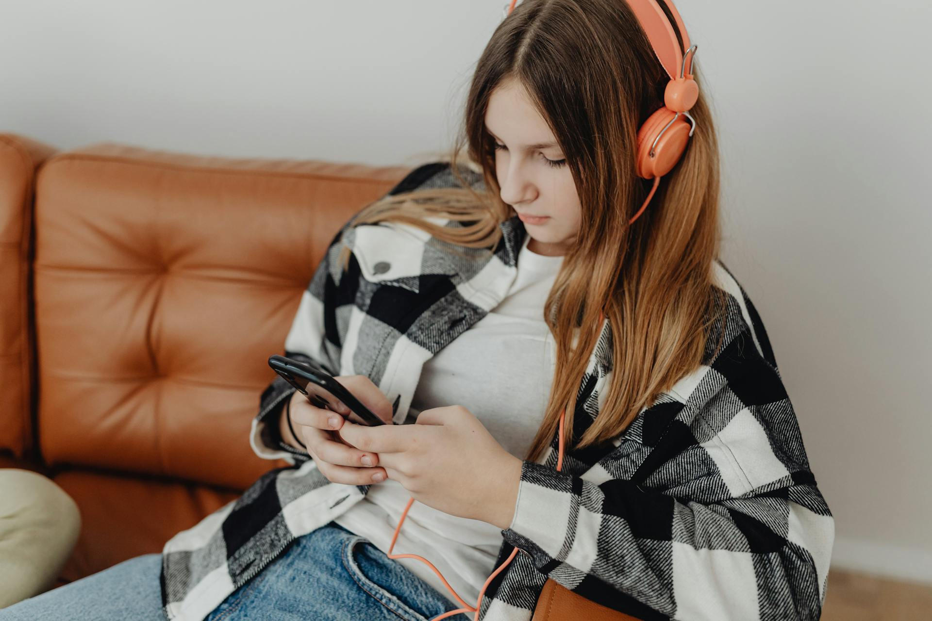 A young girl wearing headphones and using her phone | Source: Pexels