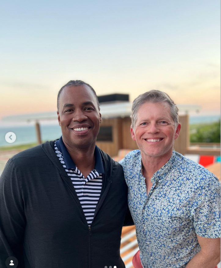 Jason Collins and Brunson Green smile together during a sunset gathering near the water, posing outdoors in casual patterned shirts with the ocean in the background. | Source: Instagram/jasoncollins_98