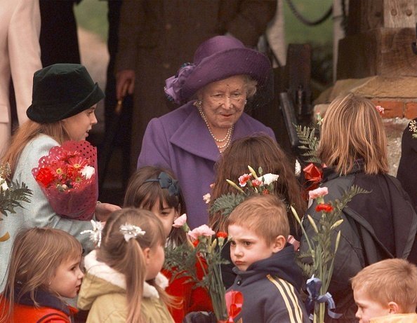 The Queen Mother (centre) is assisted by her great-grandaughter Princess Beatrice (left) as she recieves flowers from children after the Christmas Day Church Service at the Sandringham Estate. * The Royal family traditionally spend the Christmas period on their estate in Norfolk, eastern England | Photo: Getty Images