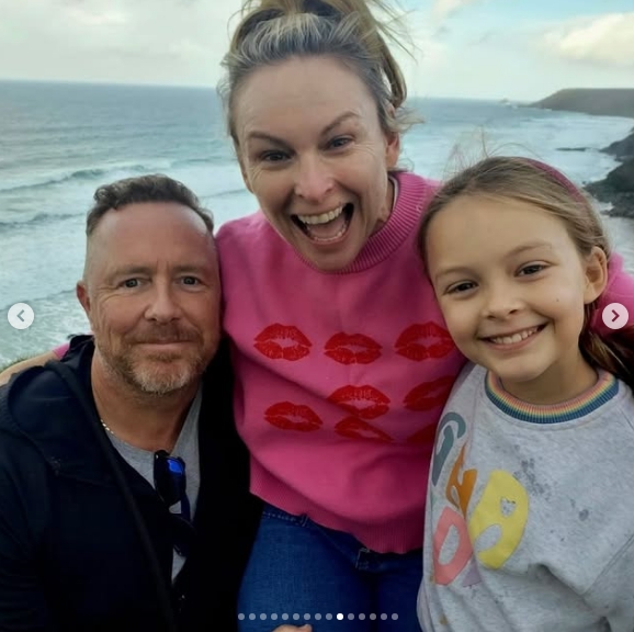 Mel Schilling beaming with her husband and daughter against a coastal backdrop. | Source: Instagram/mel_schilling1