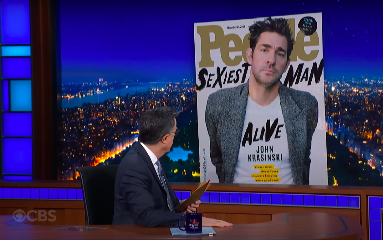 Stephen Colbert looking at People magazine's cover photo of John Krasinski during an episode of "The Late Show with Stephen Colbert," posted on November 13, 2024 | Source: YouTube/The Late Show with Stephen Colbert