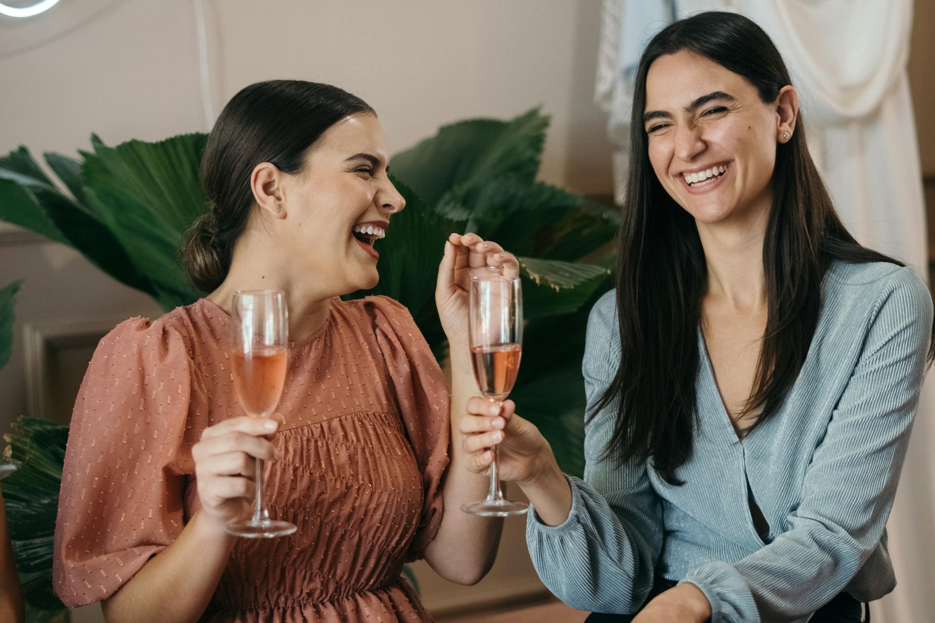 Two women laughing while holding drinks at a party | Source: Pexels