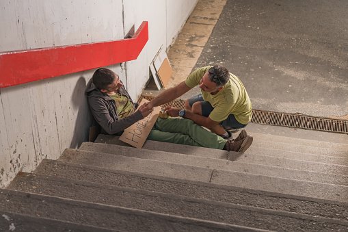  A polite and kind man is pictured helping a homeless person who is sitting on the stairs in the city underground | Photo: Getty Images