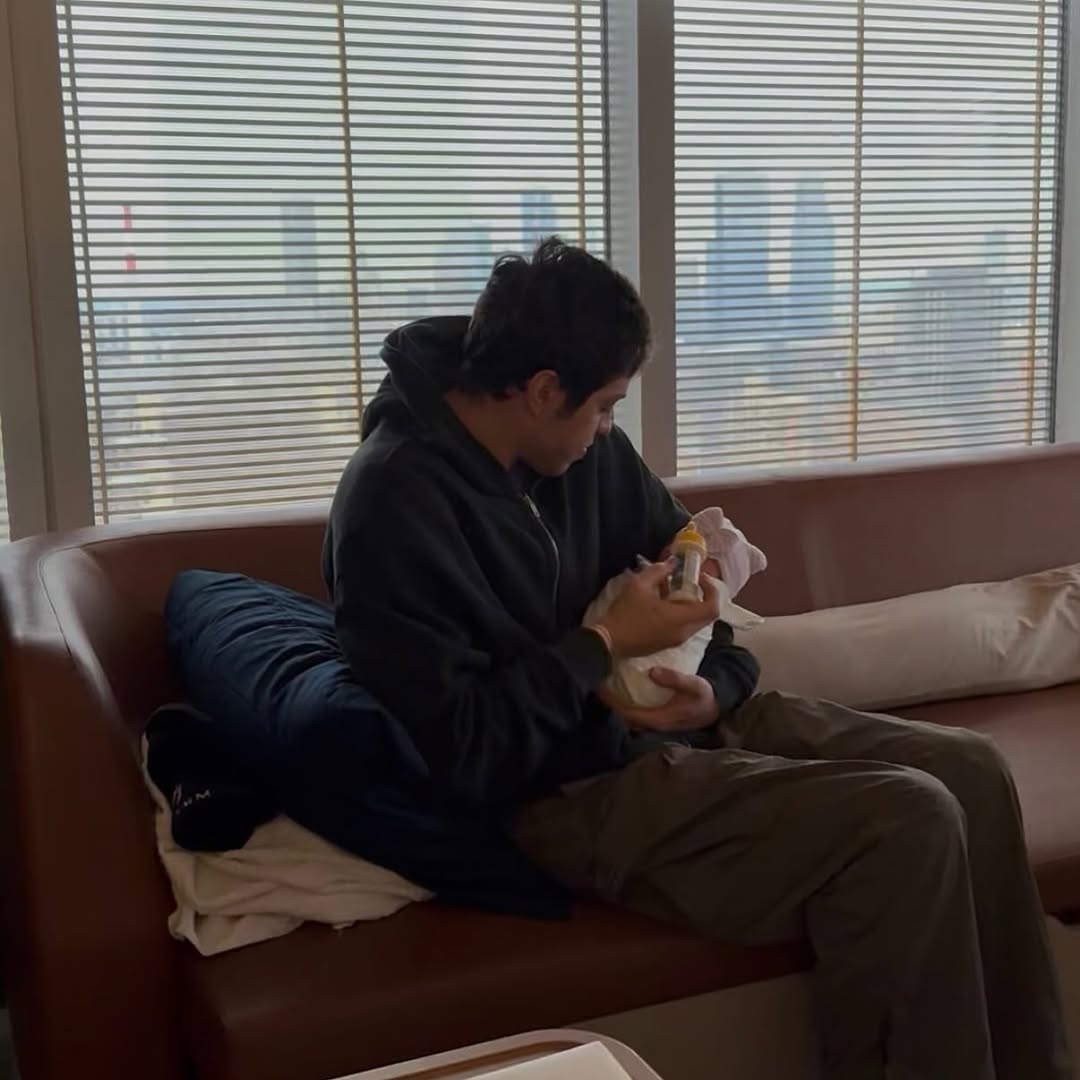 Pete Davidson feeds Scottie Rose with a bottle while seated by a large window with a city view, as posted on December 18, 2025 | Source: Instagram/elsie