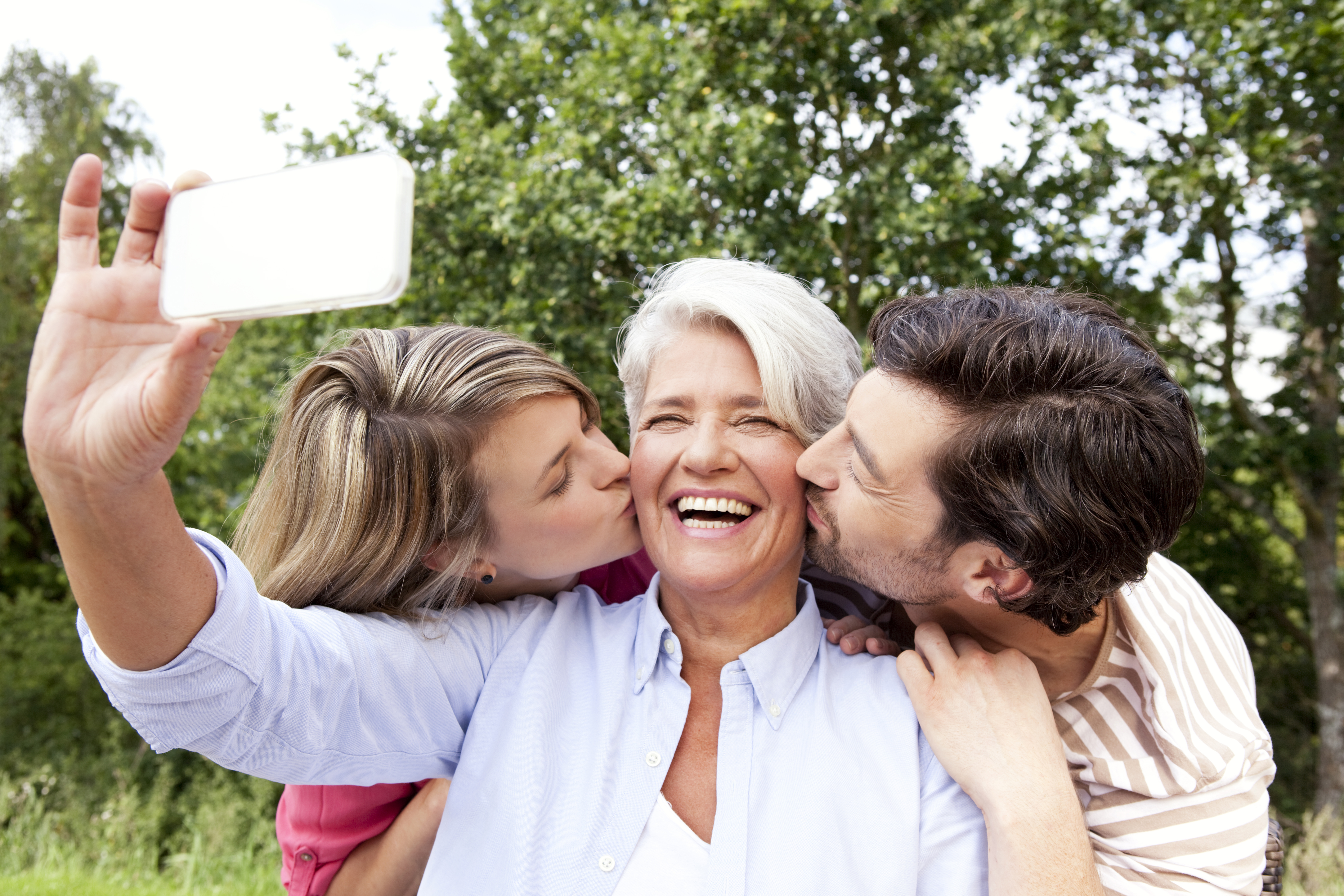 An older woman taking a selfie while getting kisses from a couple | Source: Getty Images