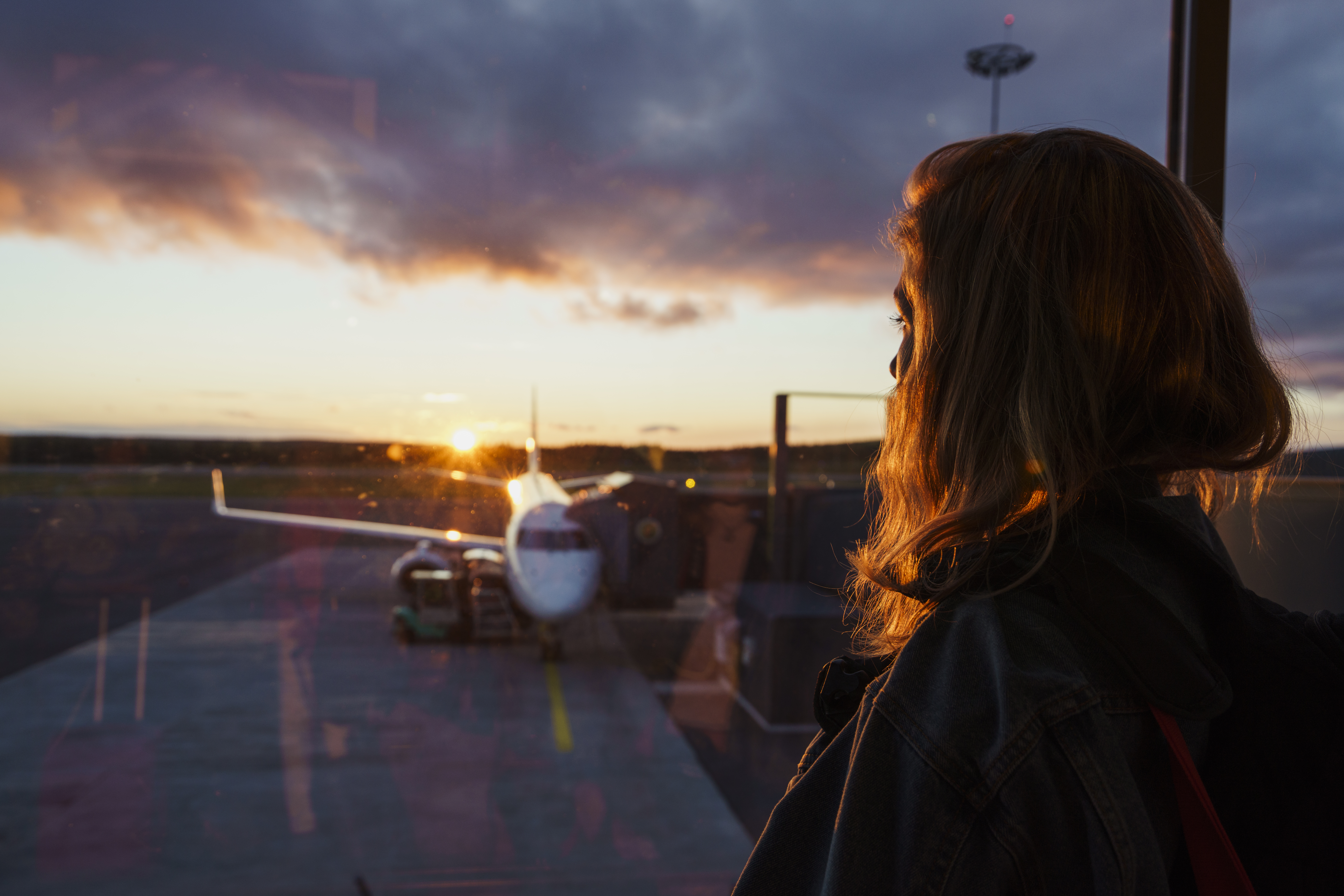 Young woman looking through window on plane at the airport at sunset | Source: Getty Images