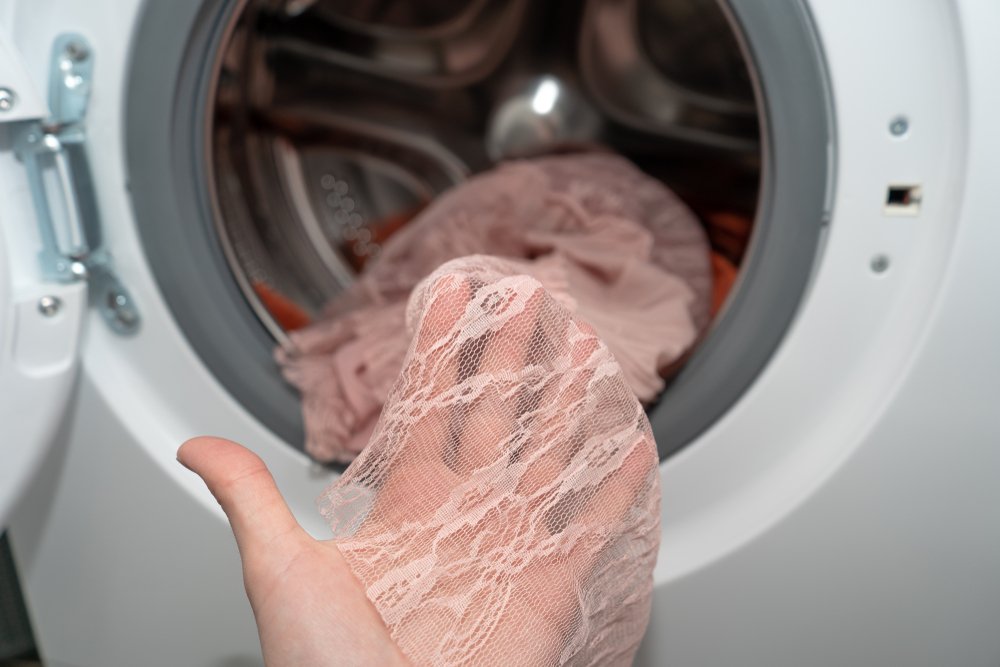 Mujer sosteniendo una prenda de ropa transparente frente a una lavadora. | Foto: Shutterstock