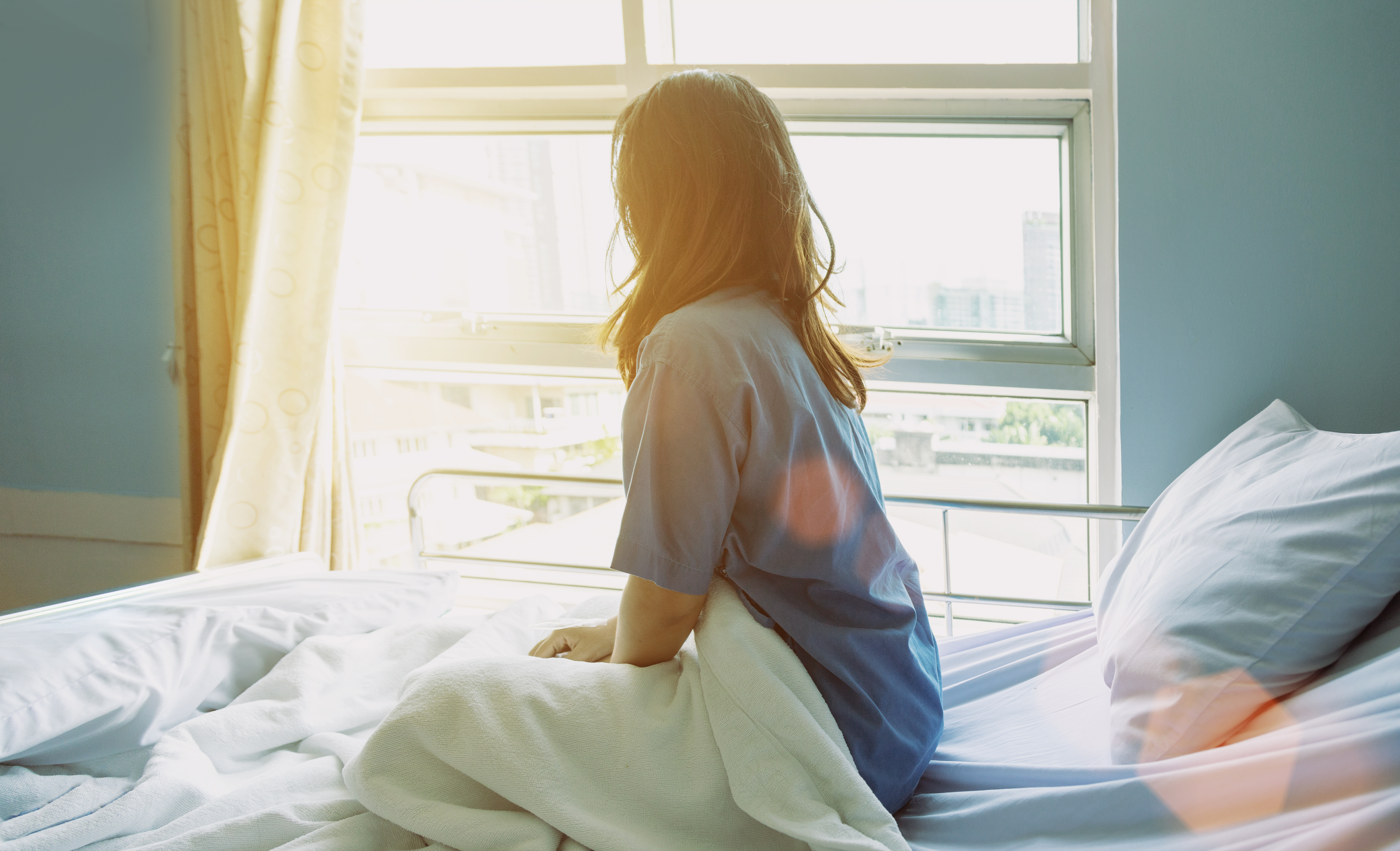 A woman looks outside a window while sitting on a hospital bed | Source: Shutterstock