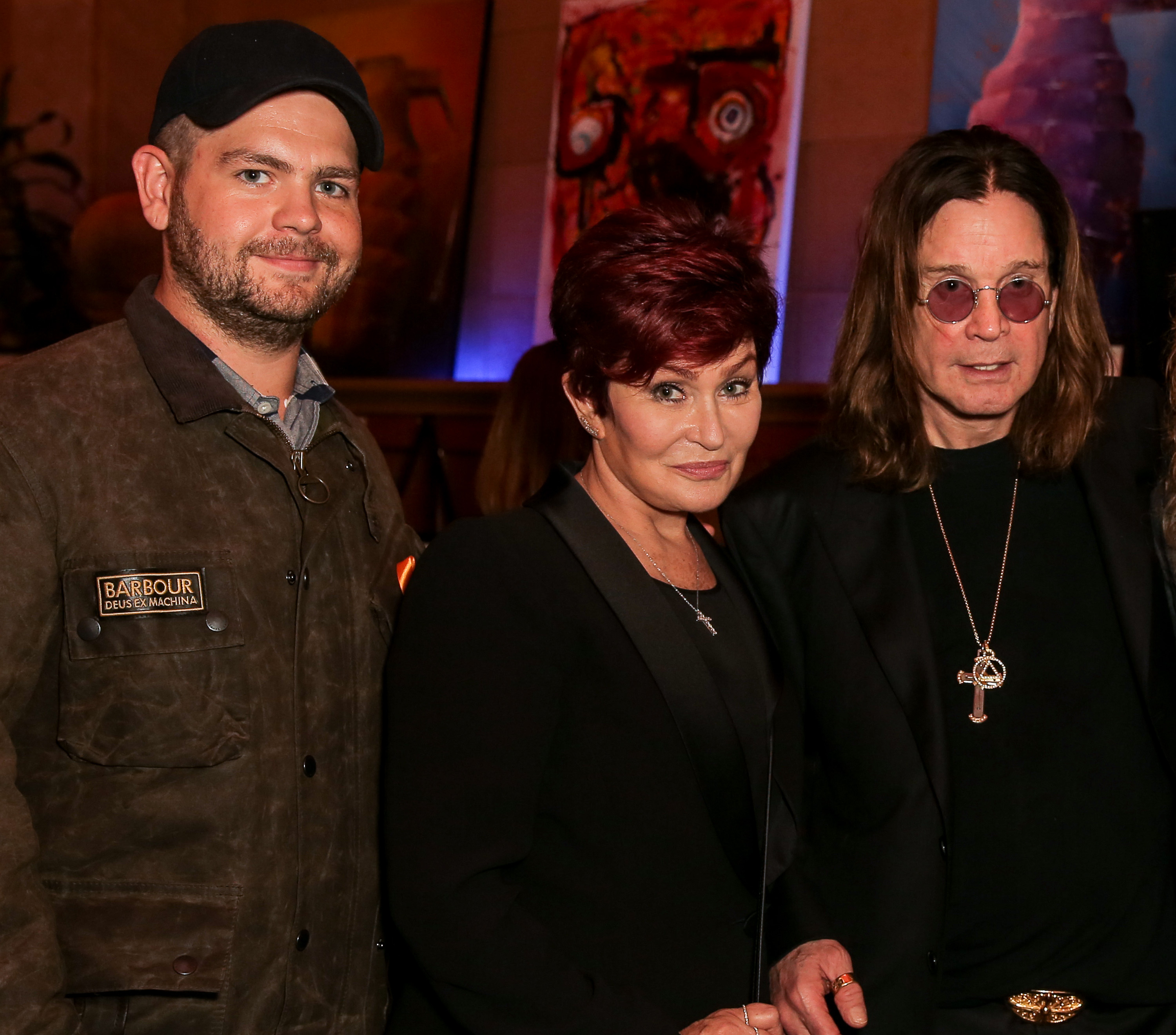 Jack Osbourne joins his parents Sharon and Ozzy for a photo at an event in Los Angeles, the trio standing close together in front of a display of vibrant artwork.