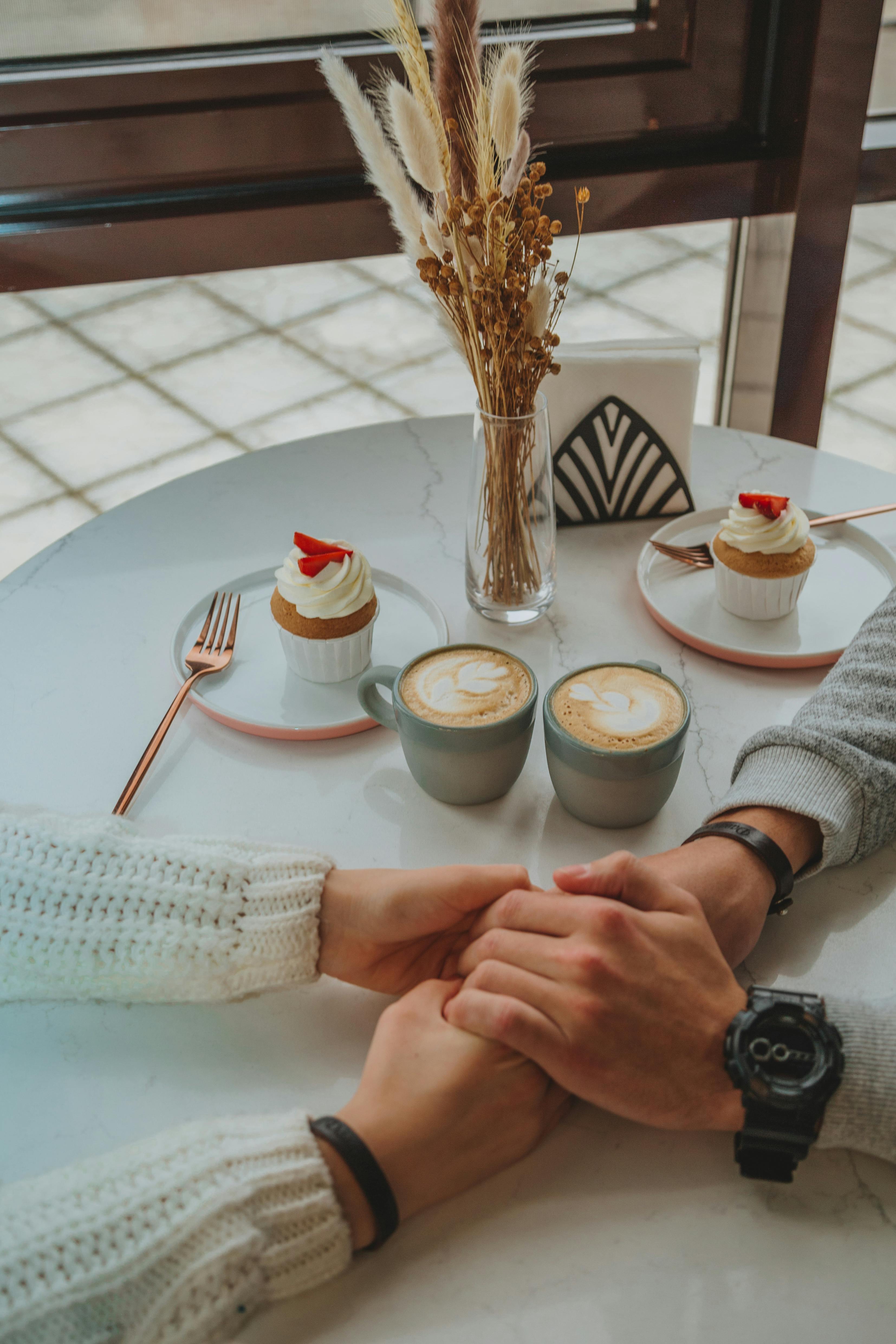 A couple holding hands while enjoying dessert and coffee | Source: Pexels