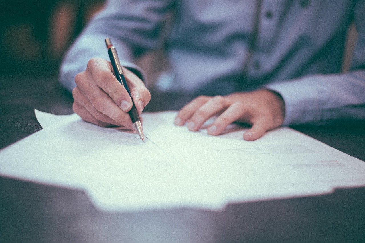 A middle aged man writing a handwritten letter on a desk. I Image: Pixabay.