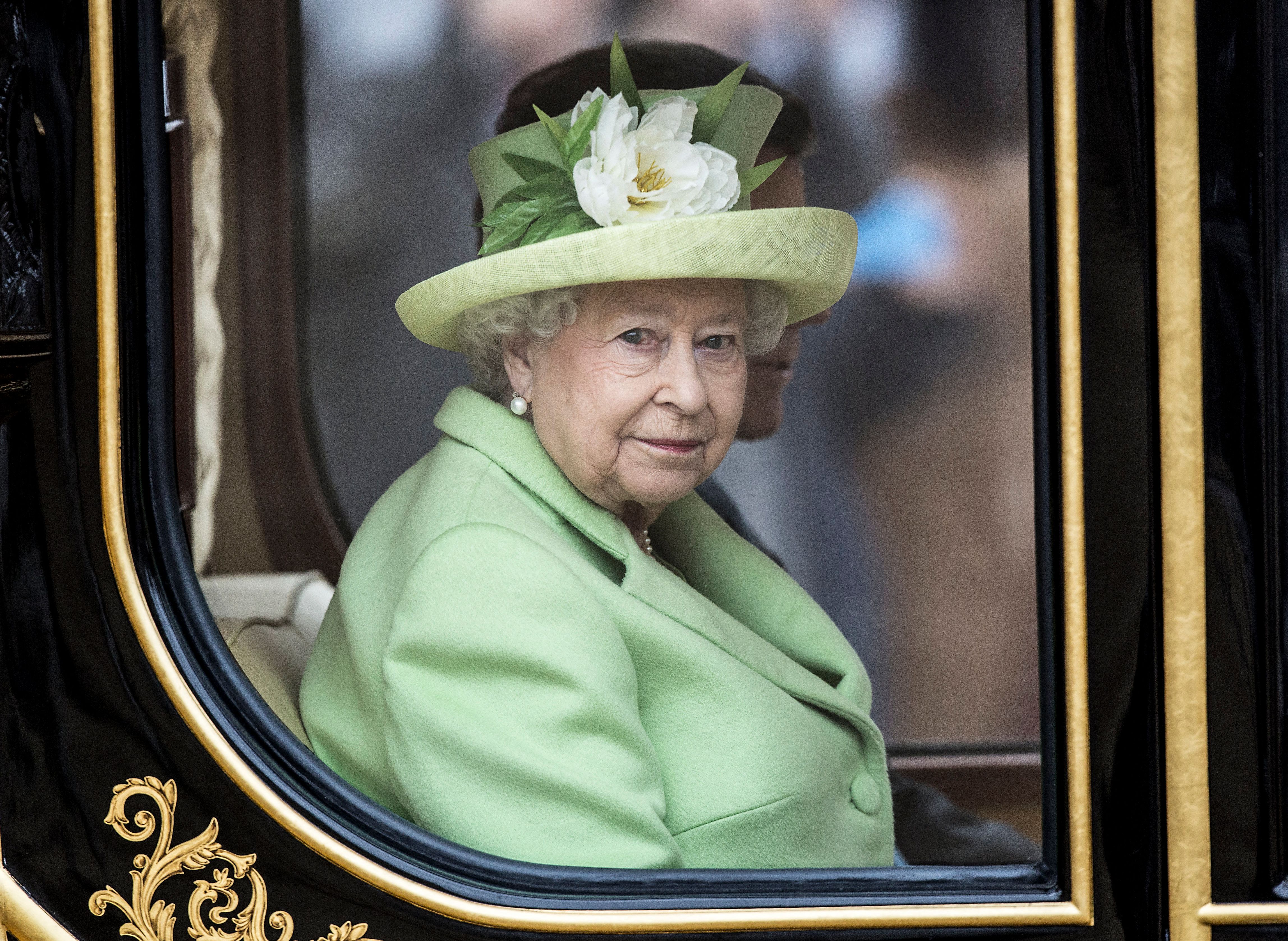 Seated inside the Diamond Jubilee State Coach, Queen Elizabeth II travels with former Colombian President Juan Manuel Santos during his state visit to the United Kingdom in 2016. Wearing green with a floral hat, the monarch's red eye is subtly apparent through the carriage window.