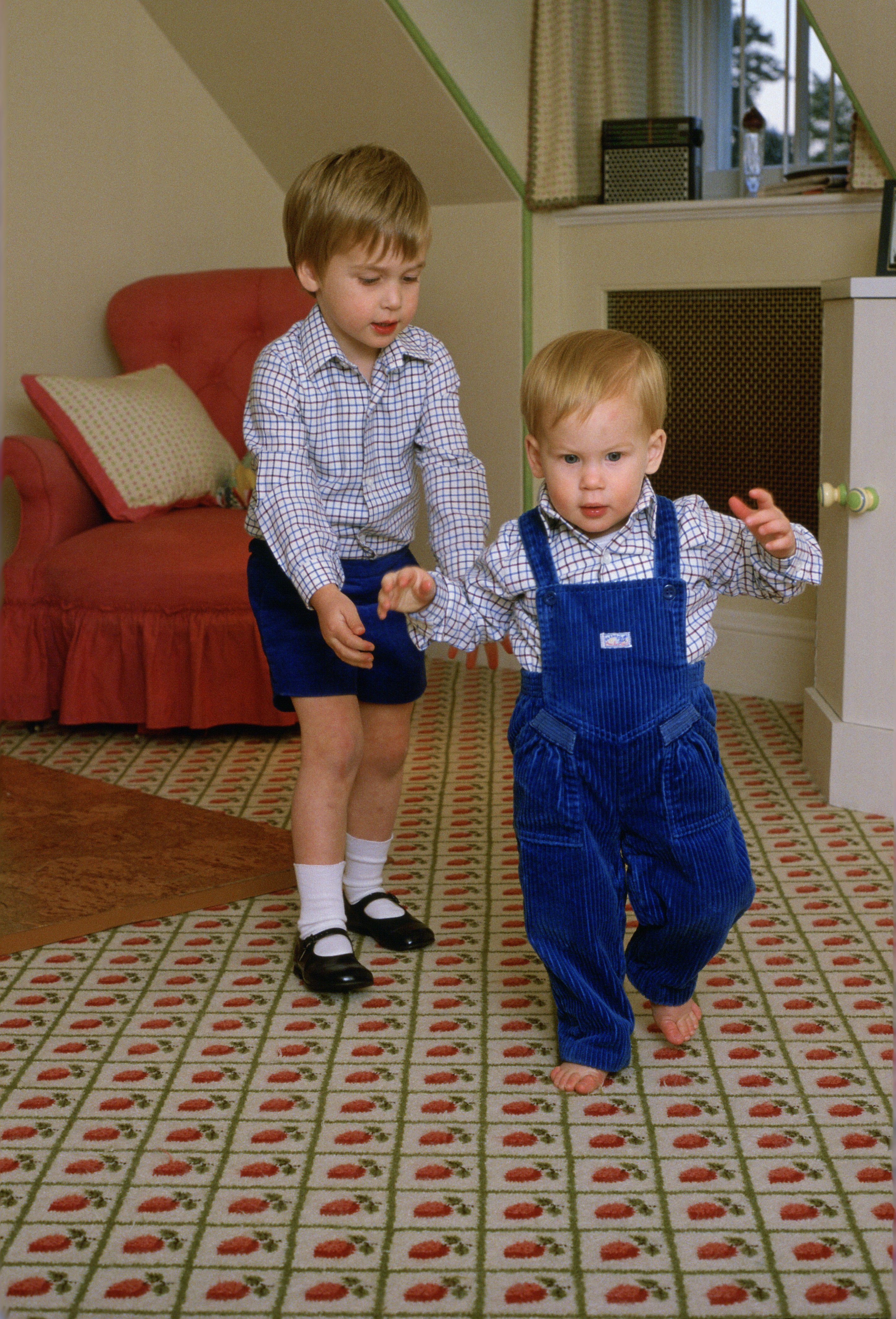 Prince William and Prince Harry as the latter tries to walk on his own in the playroom at Kensington Palace on October 22, 1985. | Source: Getty Images