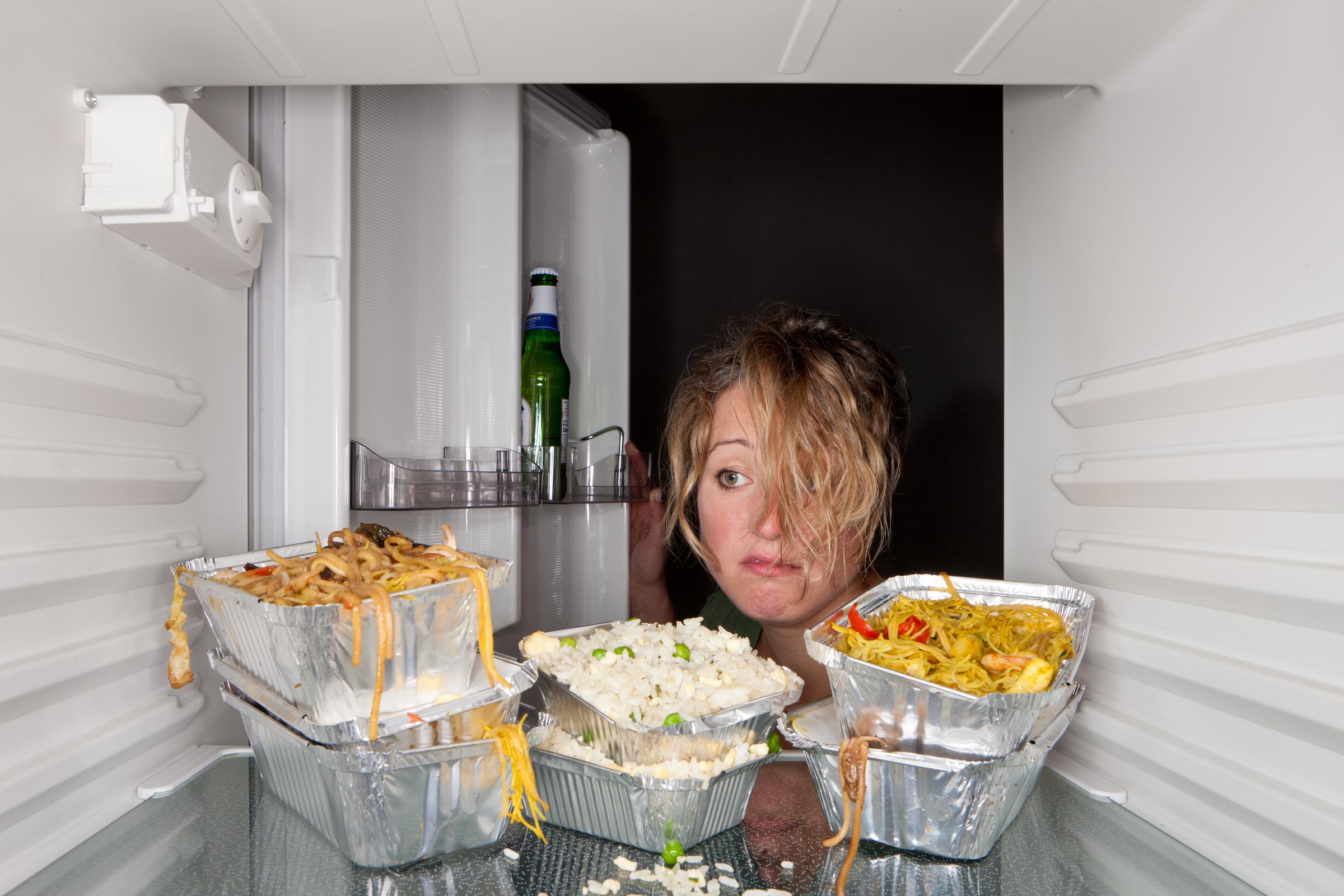 A woman looking at old take-away food containers left in a refrigerator | Source: Getty Images