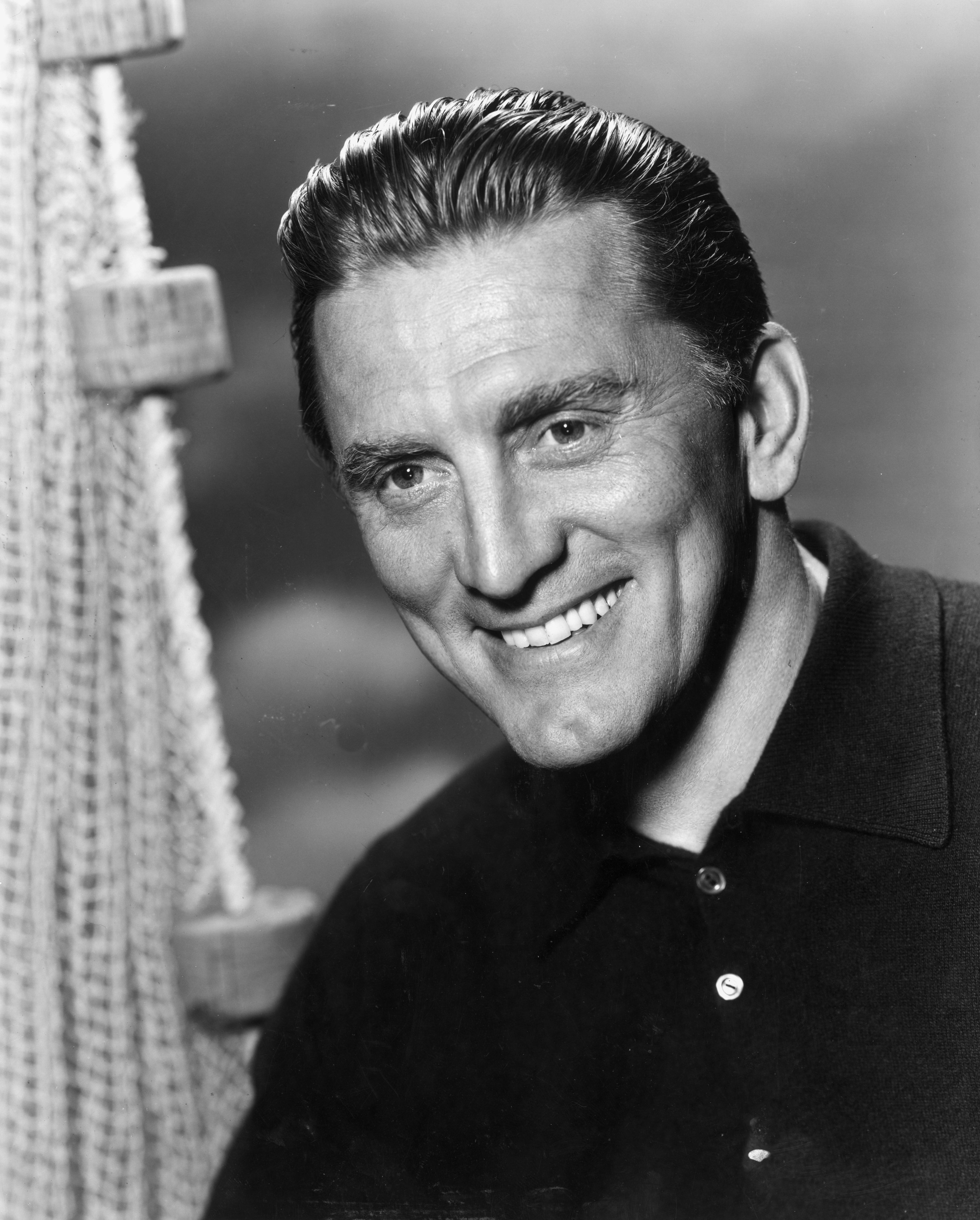 Humanitarian Kirk Douglas pictured broadly smiling while donning a black golf shirt. / Source: Getty Images