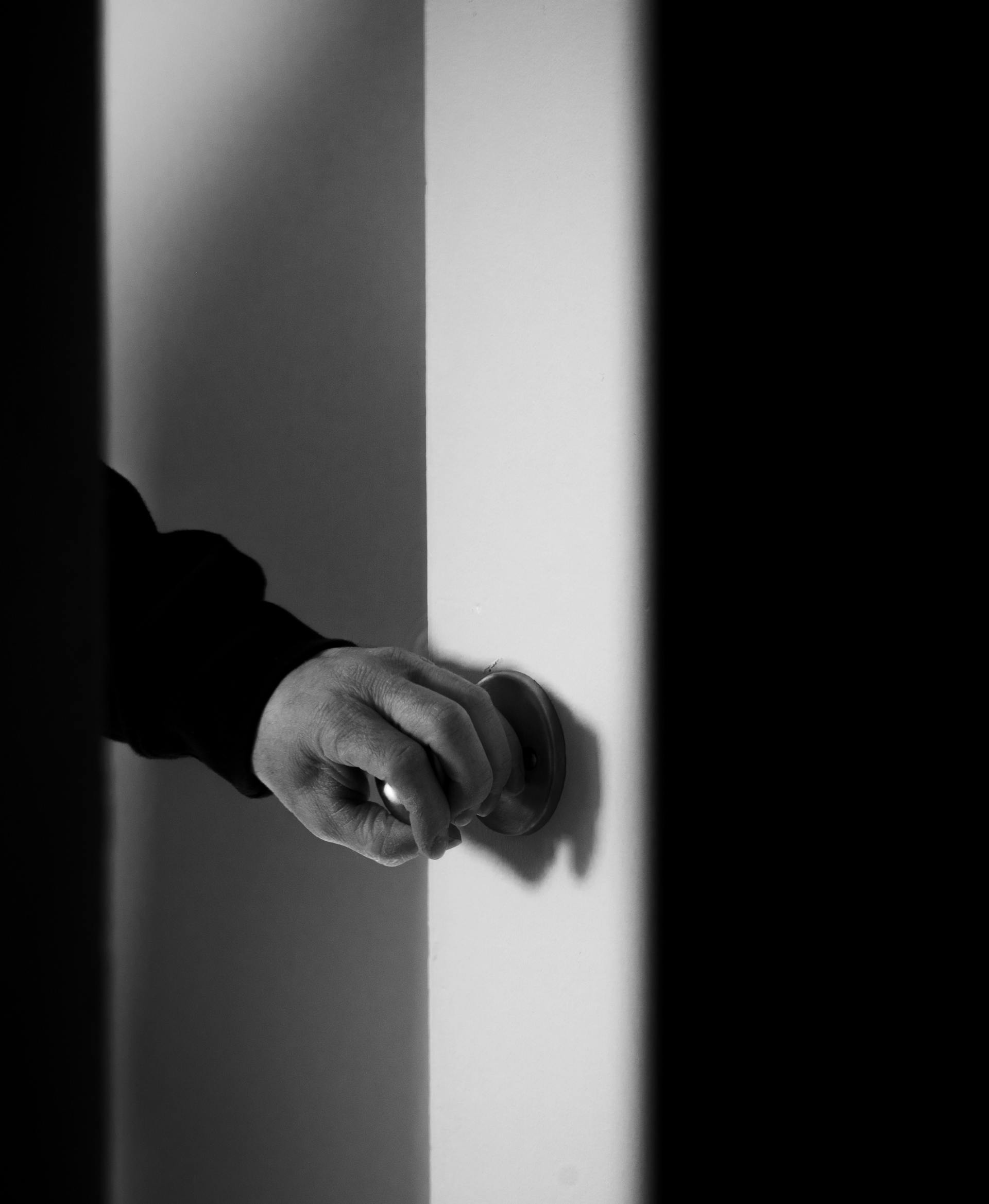 Grayscale close-up of a man's hand on a doorknob | Source: Pexels