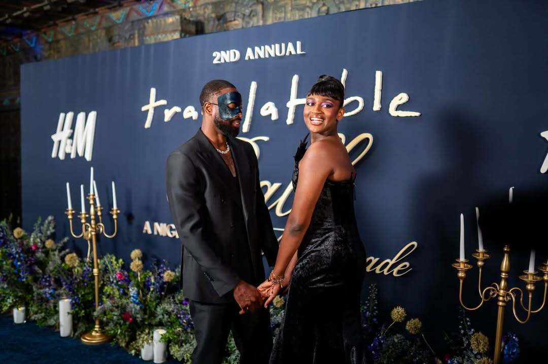 Zaya Wade smiles over her shoulder while holding hands with a masked guest, posing amid candlelit décor and floral arrangements at the Translatable Ball. | Source: Instagram/translatableproject