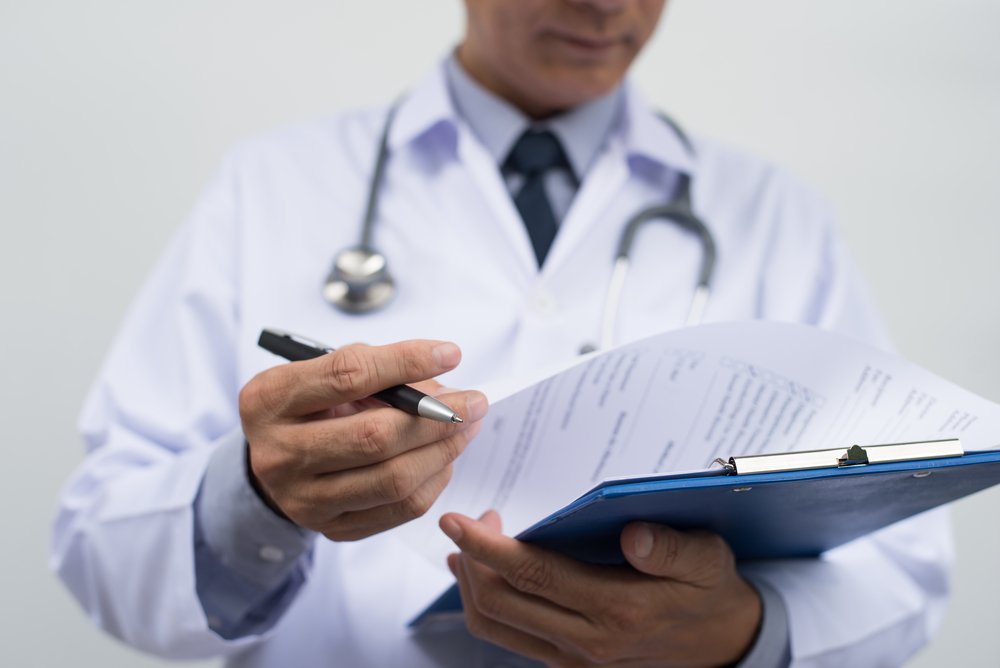 Male doctor in white coat looking over medical documents.| Source: Shutterstock