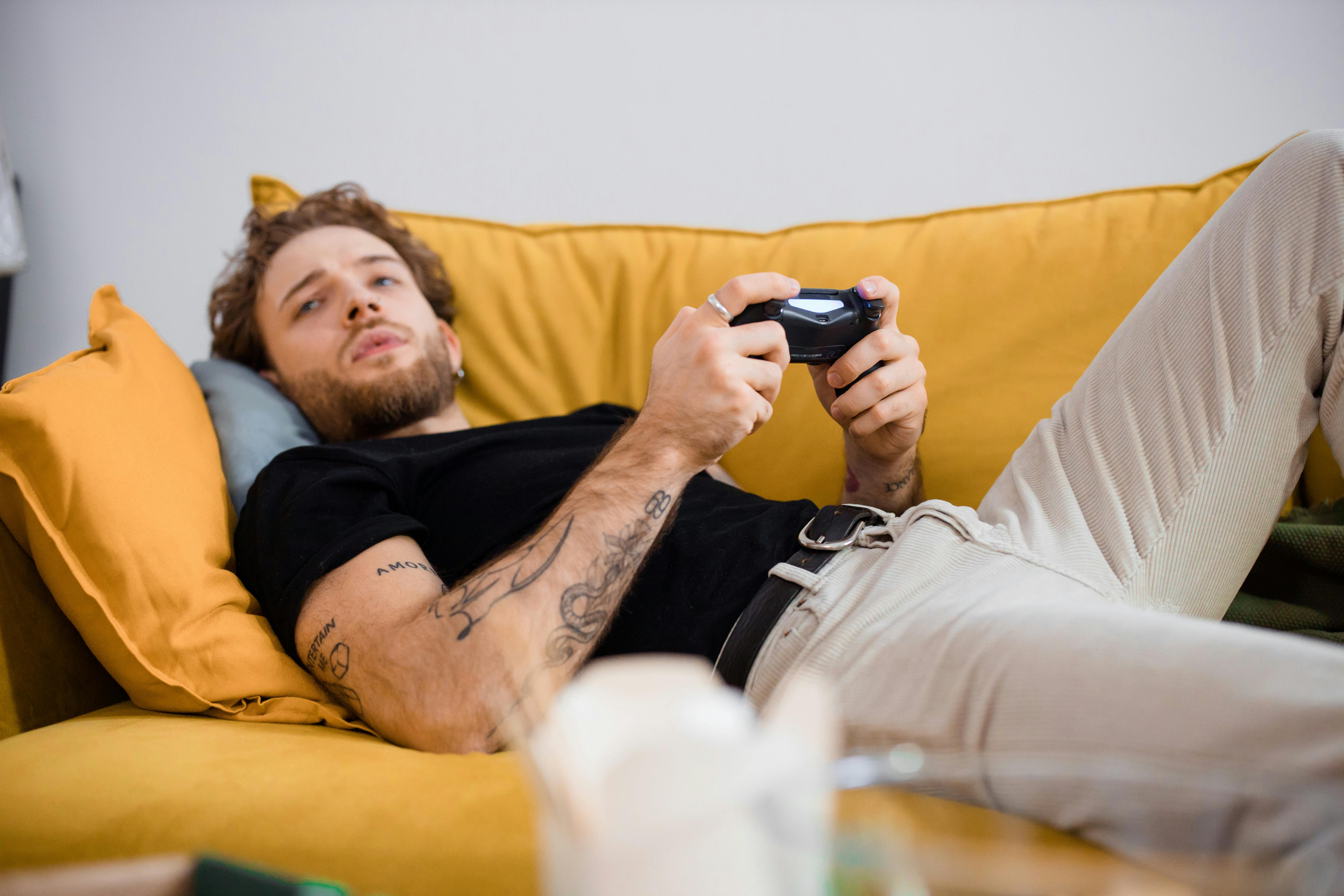 A man playing a television game while lying on a couch | Source: Pexels